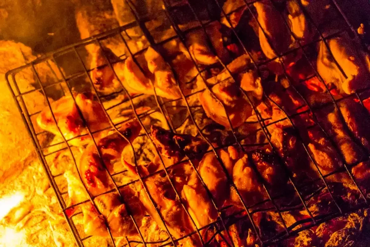 Chicken pieces grilling over an open flame in a barbecue grill.