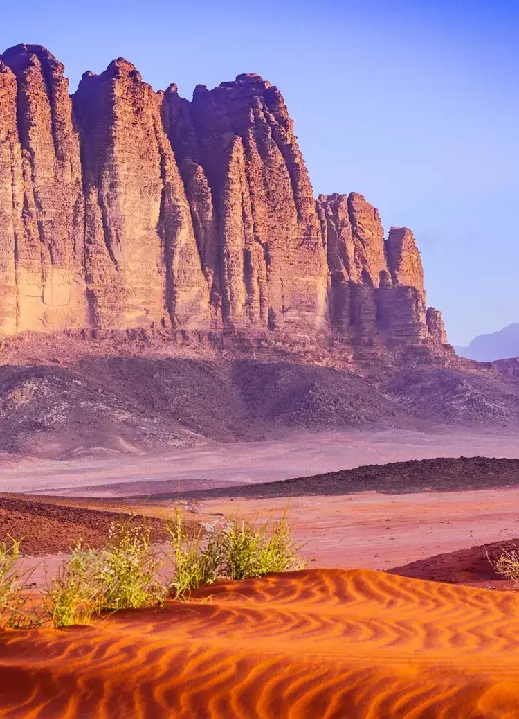 Rock formations and sand dunes in a desert landscape with a clear blue sky.