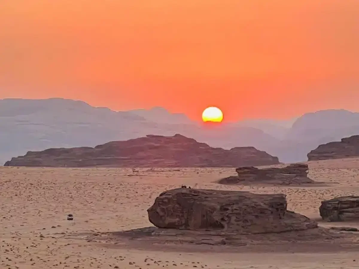 Sunset over a desert with rocky formations and sand dunes.