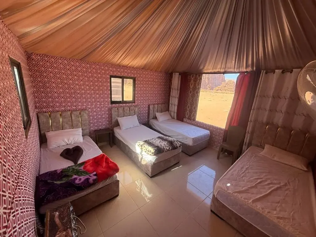 Inside a tent with multiple beds and patterned walls, with a large window showing a desert landscape outside.