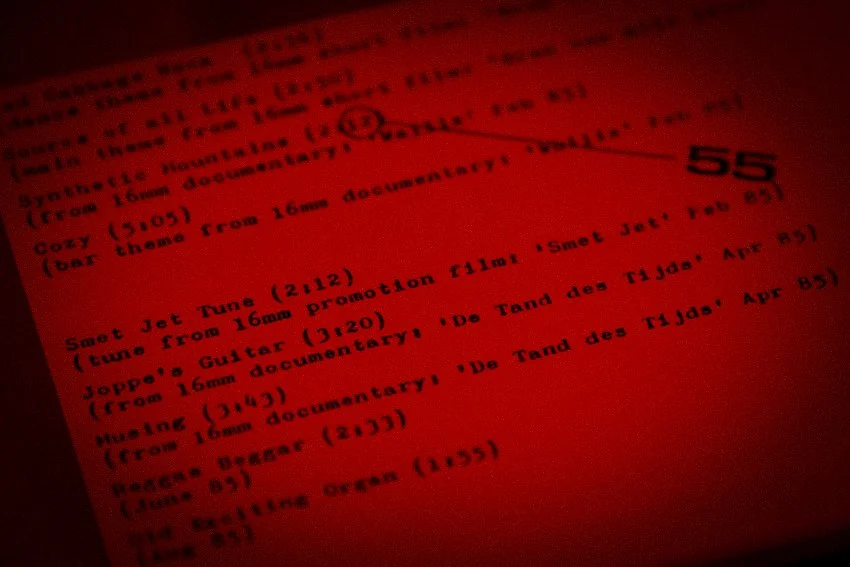 Close-up van een roodgeschilderd document met tekst over muziek, inclusief titels en tijden van nummers.