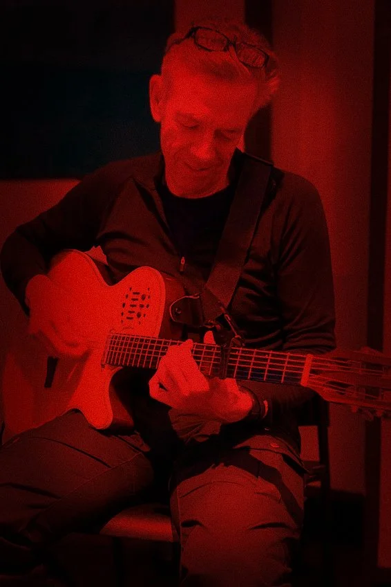 Man die in een donkere kamer op een rode achtergrond gitaar speelt.