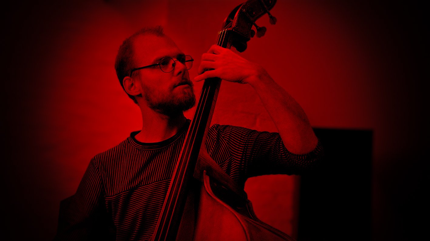 Man speelt upright bass in een donkere, rode verlichte ruimte.