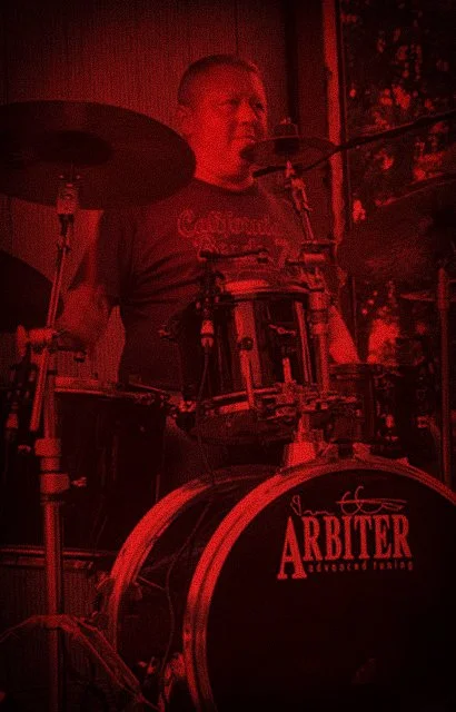Man die op een drumstel speelt, met een rood filter over de afbeelding.
