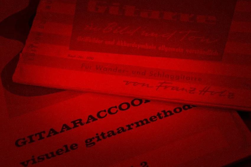 Stapel bladen of papieren, waarvan één met de tekst 'GITARAACCO' en 'visuele gitaararmethode'.