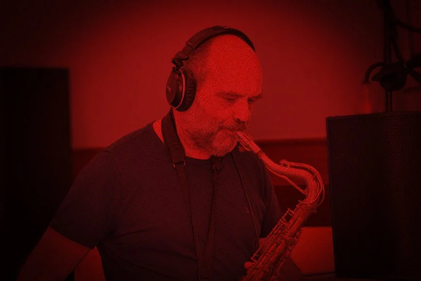 Mann met koptelefoon die saxofon speelt in een geluidsstudio, rood licht