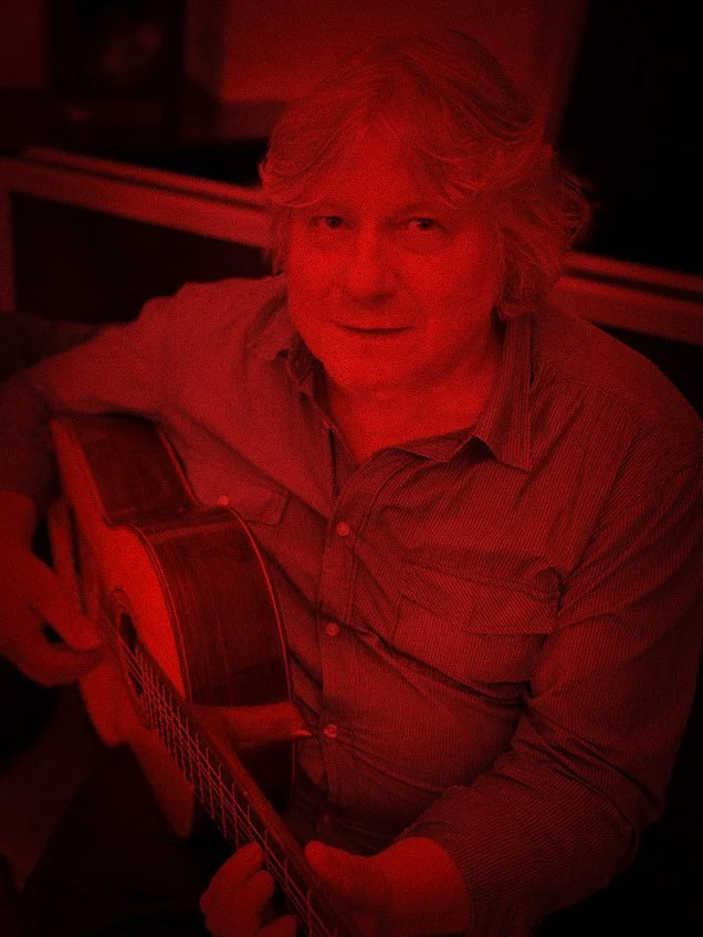 Man met grijze haar die een gitaar vasthoudt, onder rood licht