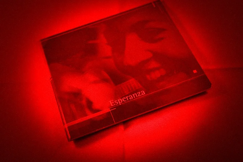 Een doos met de afbeelding van een lachende persoon en de tekst 'Esperanza', afgezet met rood licht.