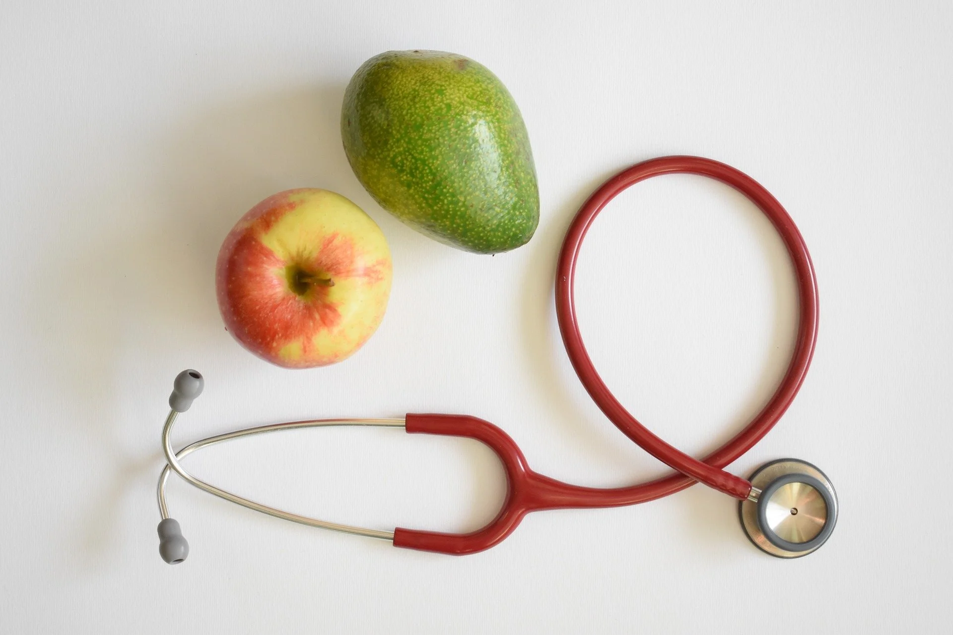 An apple, an avocado, and a stethoscope on a white background.