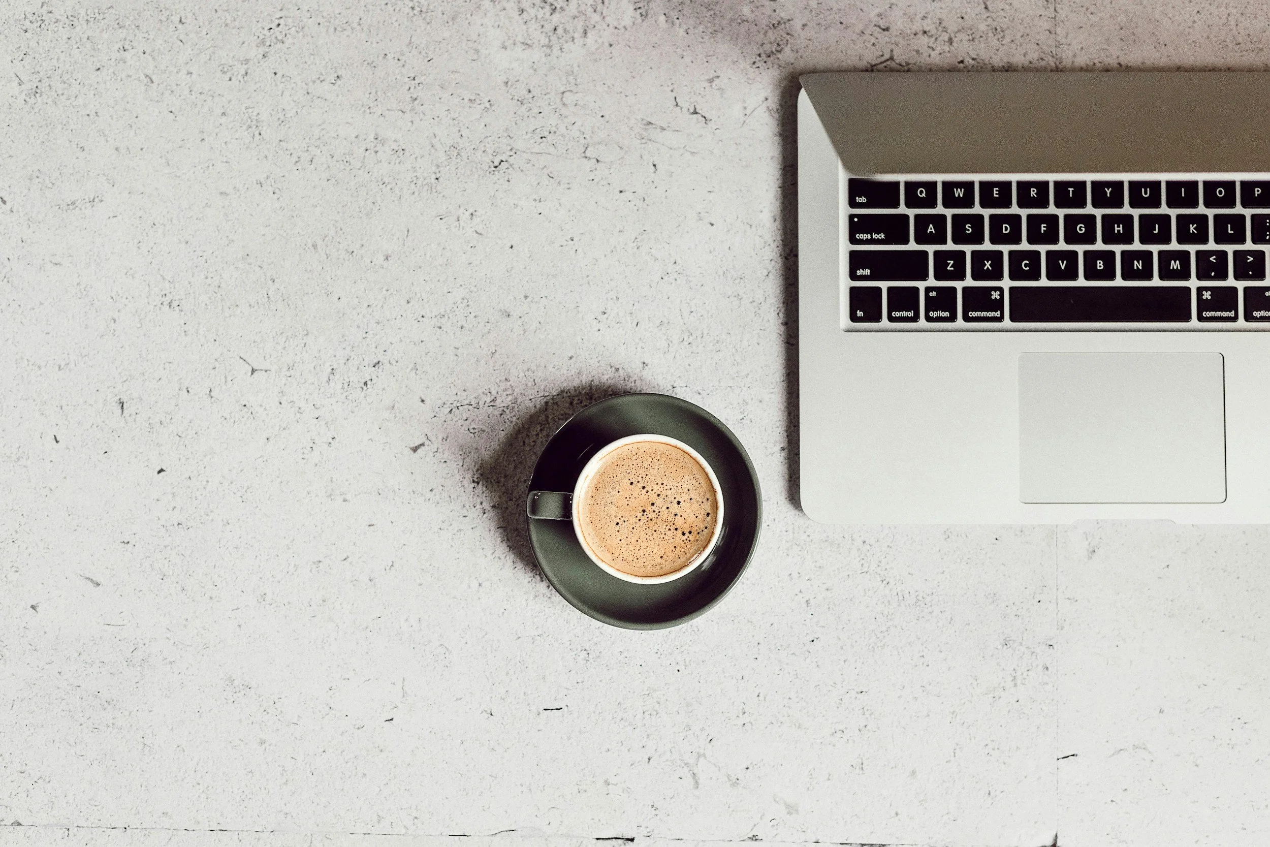 A laptop and cup of coffee on a textured white surface