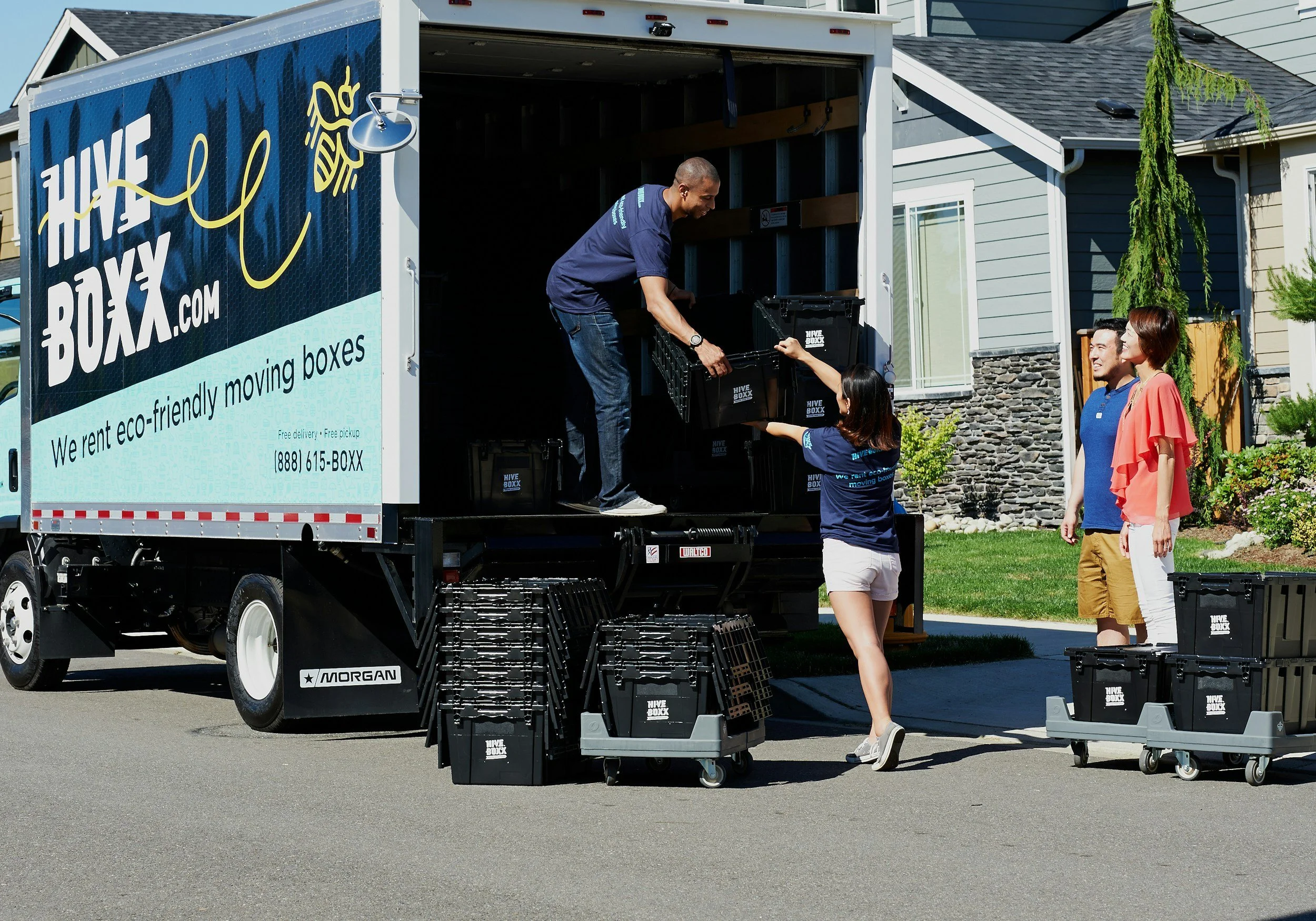 People unloading eco-friendly moving boxes from a moving truck in a residential neighborhood.
