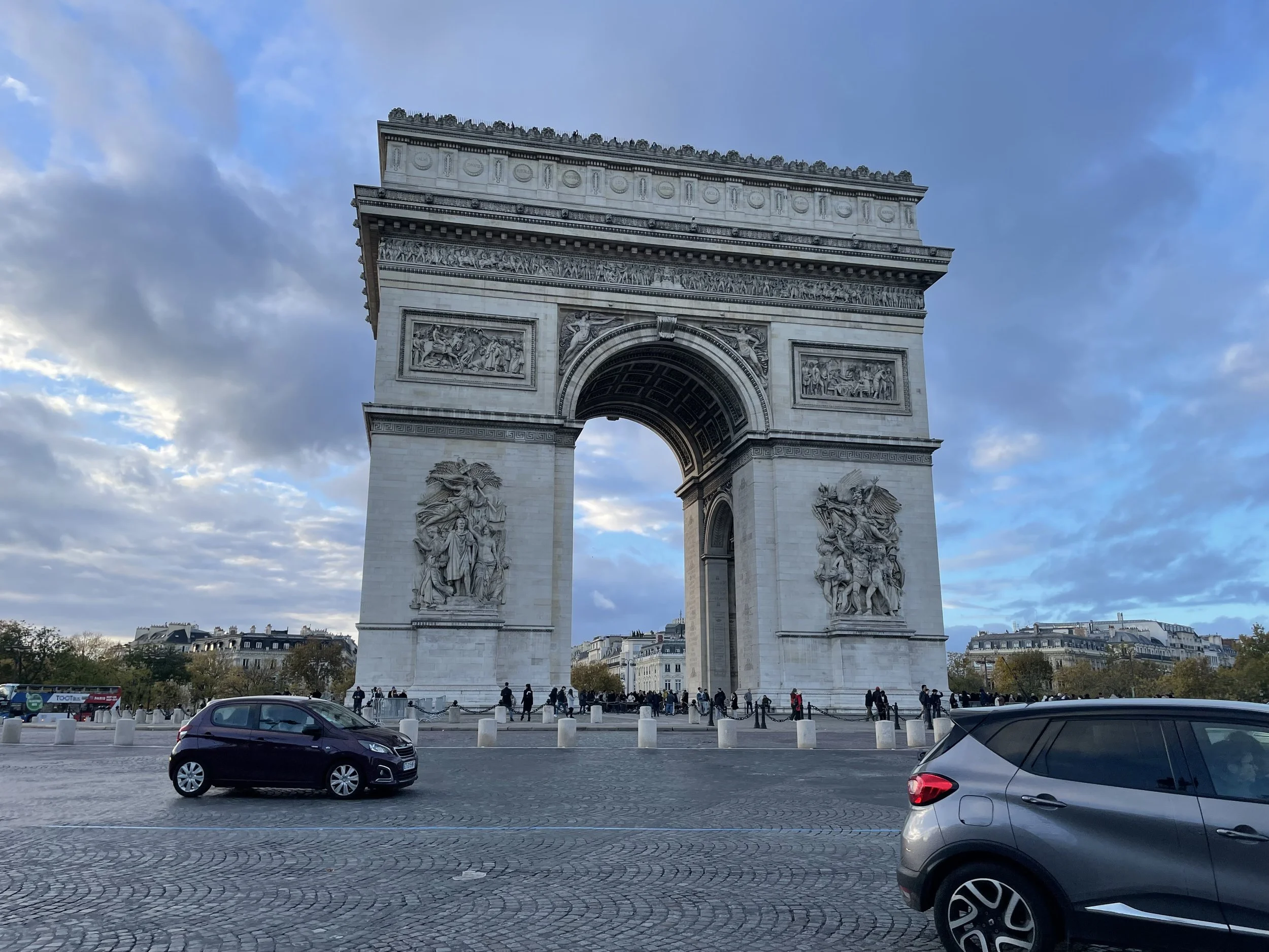 L'arc de Triomphe à Paris, France, avec des voitures au premier plan et un ciel nuageux.