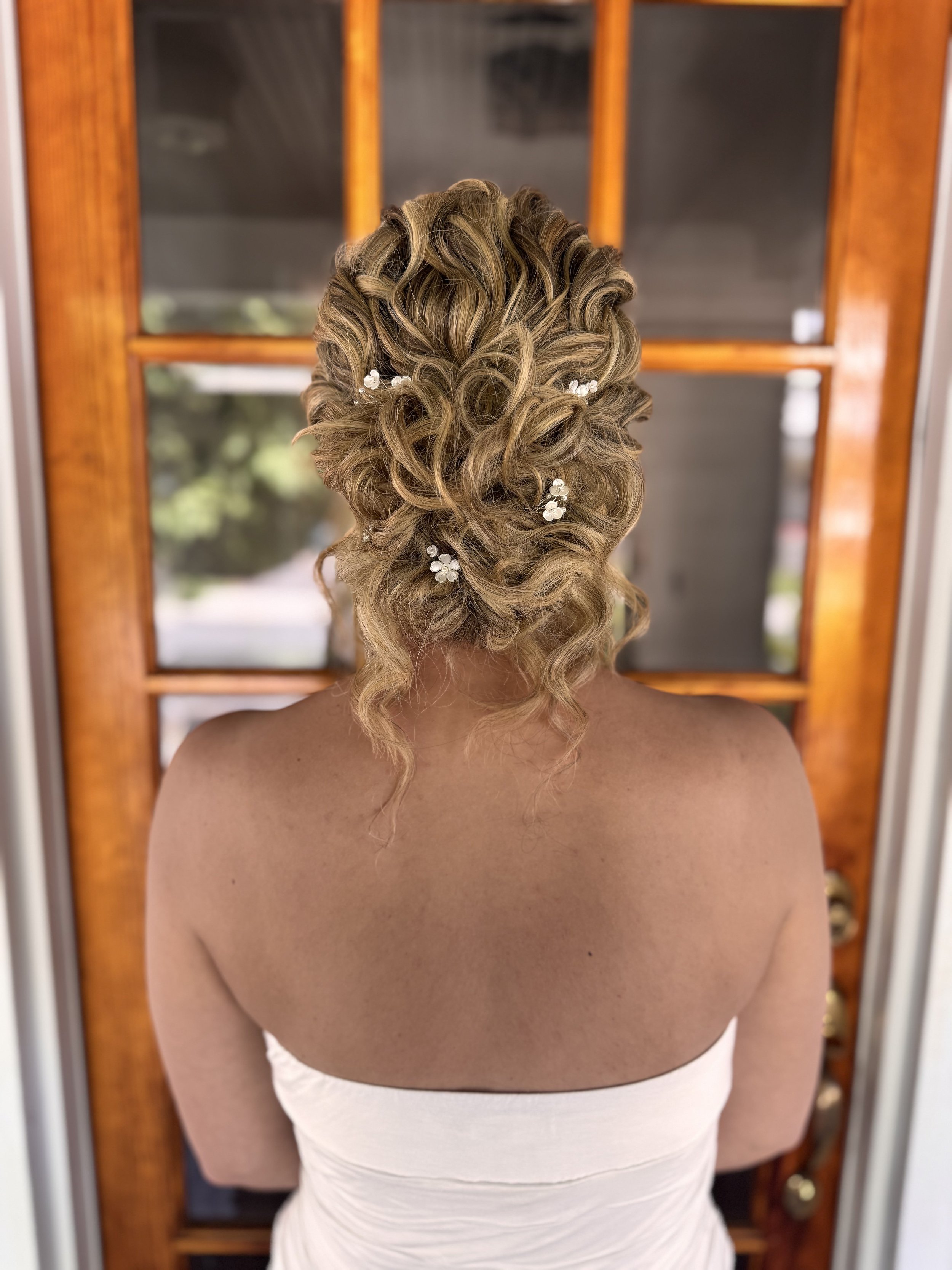Bride with curly updo and floral hairpins, wedding hair styling at Do’s & Dye in West Hartford