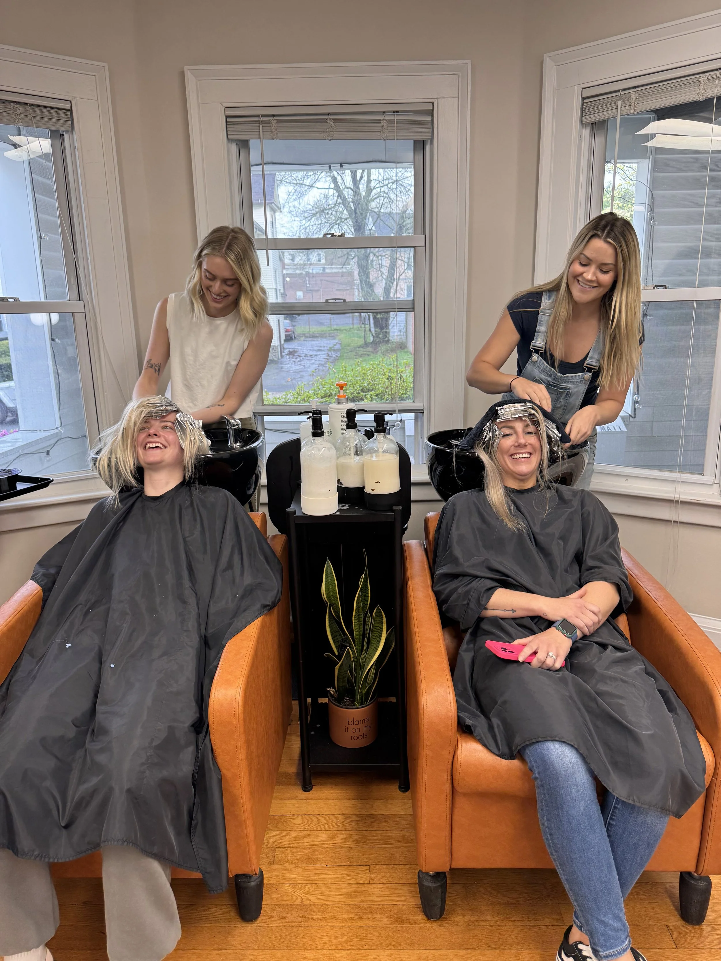 Stylists shampooing clients while they relax in salon chairs during a hair service.