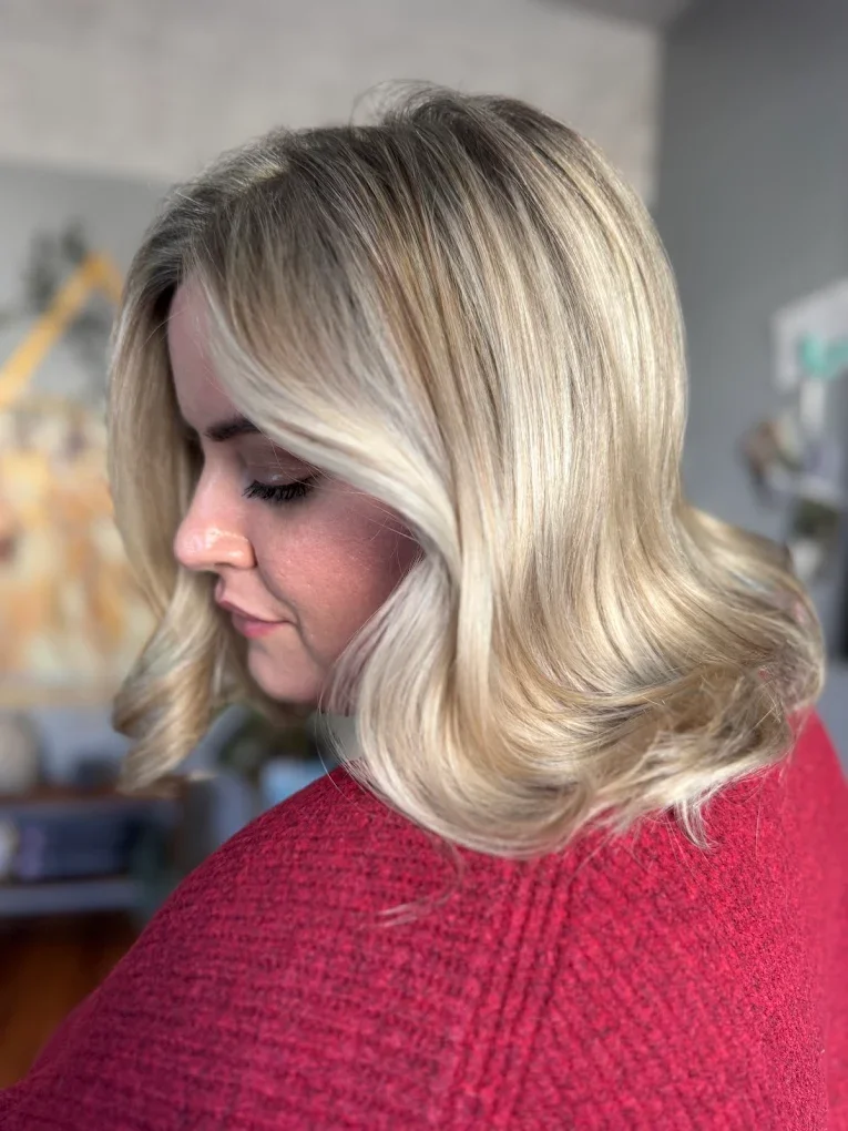 Side profile of soft, shoulder-length blonde hair styled with smooth waves and a natural finish.
