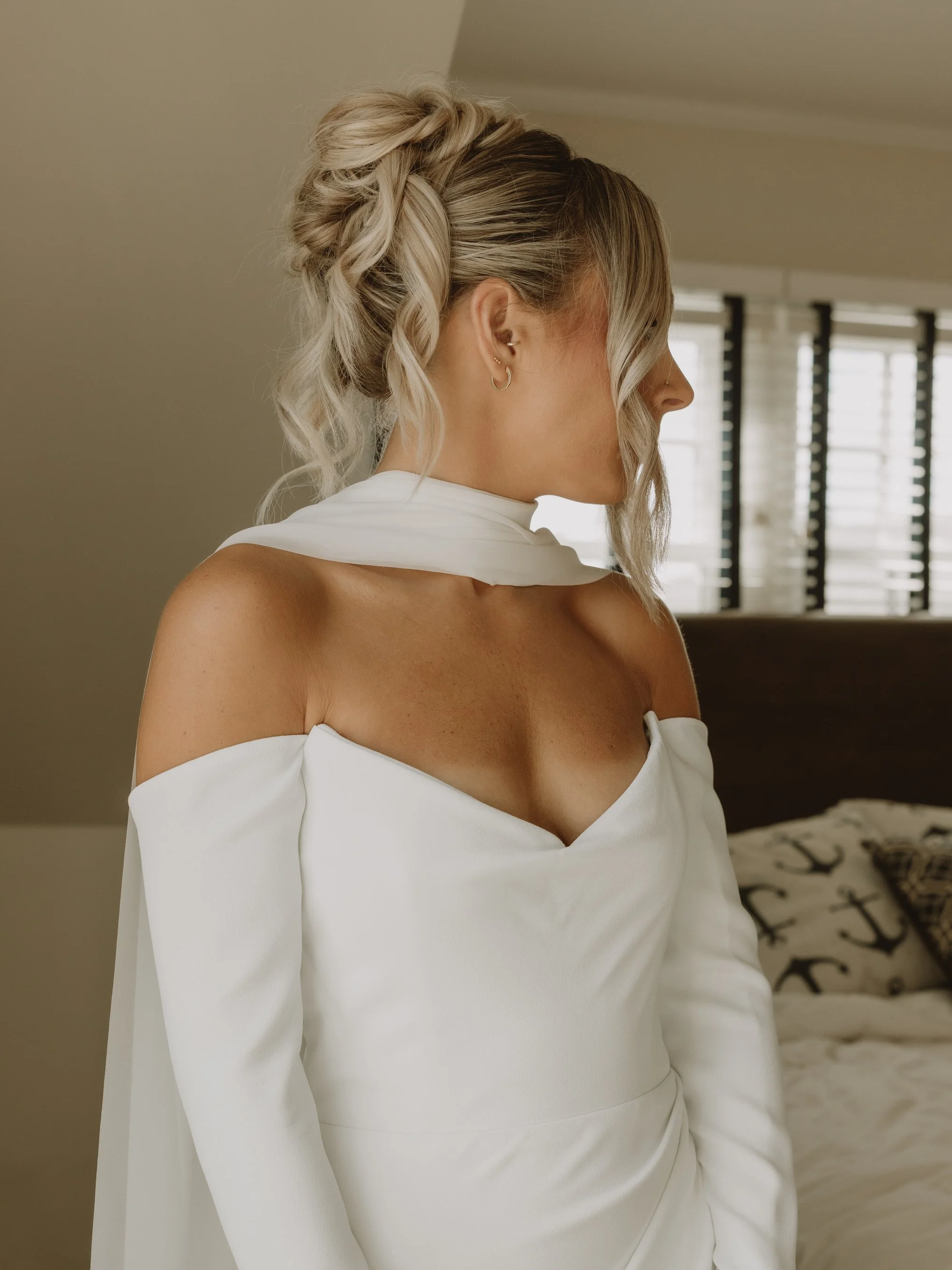 Bride in an off-the-shoulder wedding gown with an elegant low bridal updo, photographed in soft natural light.