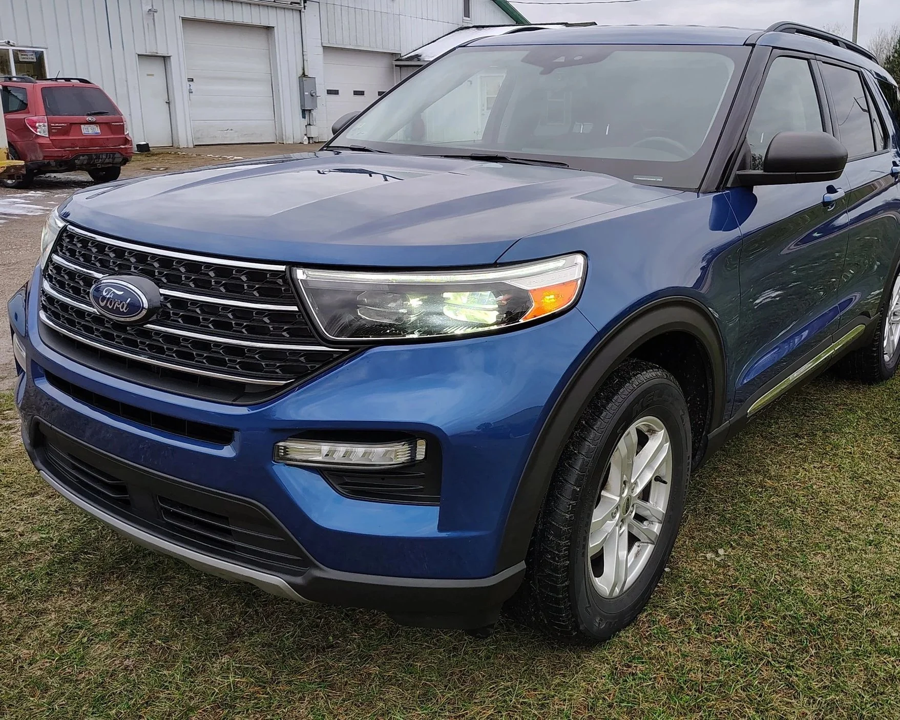 Blue Ford SUV parked on a grassy area in front of a building with garage doors.