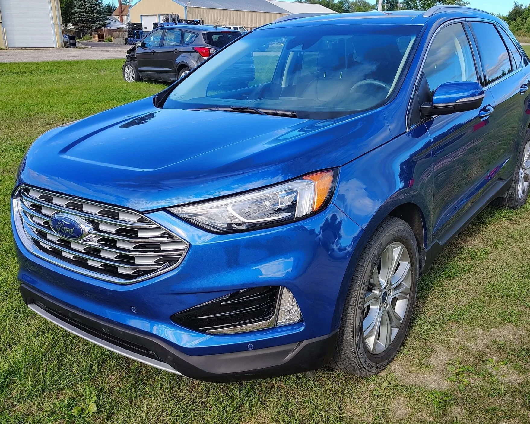 A blue Ford SUV parked on grass, with other cars and buildings in the background.