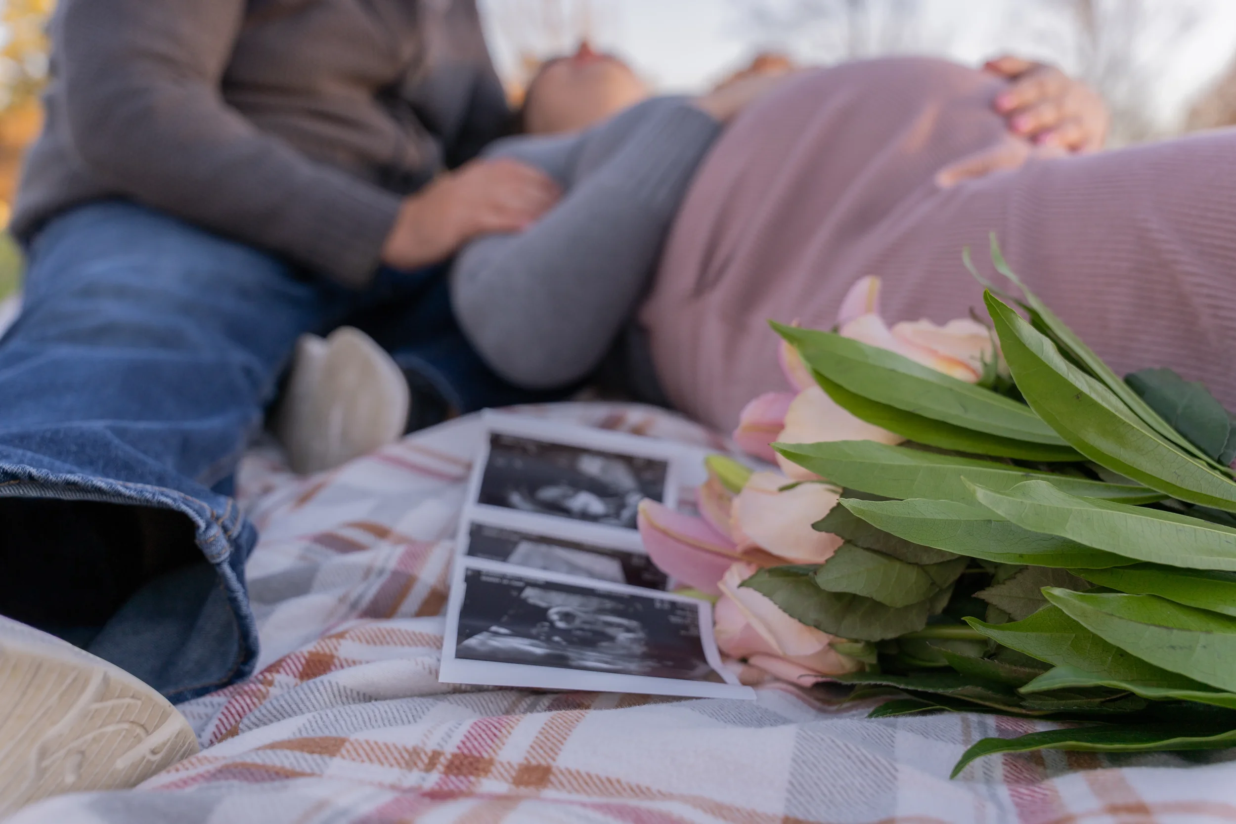 Husband and wife laying in park with ultrasound photos