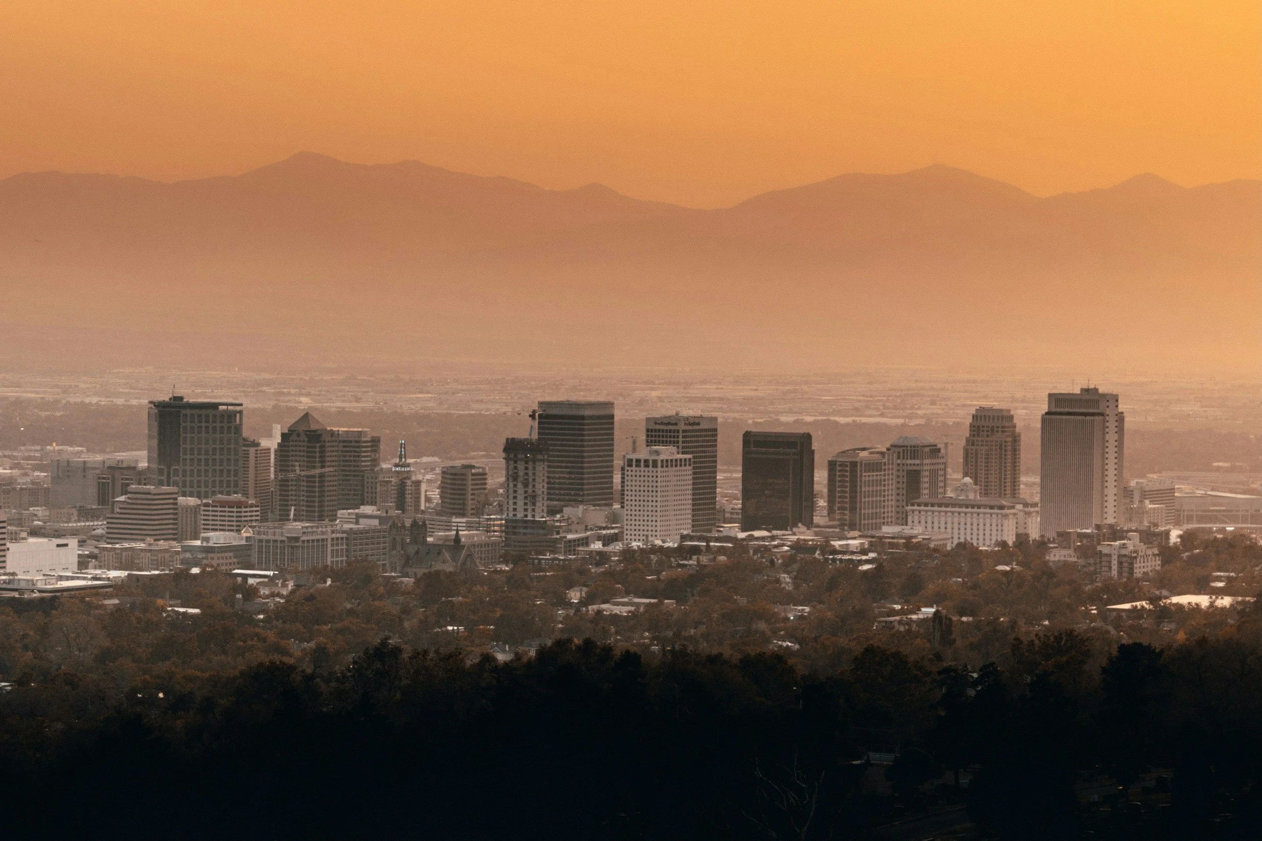 Skyline of a city with tall buildings at sunset, with mountain range in the background.