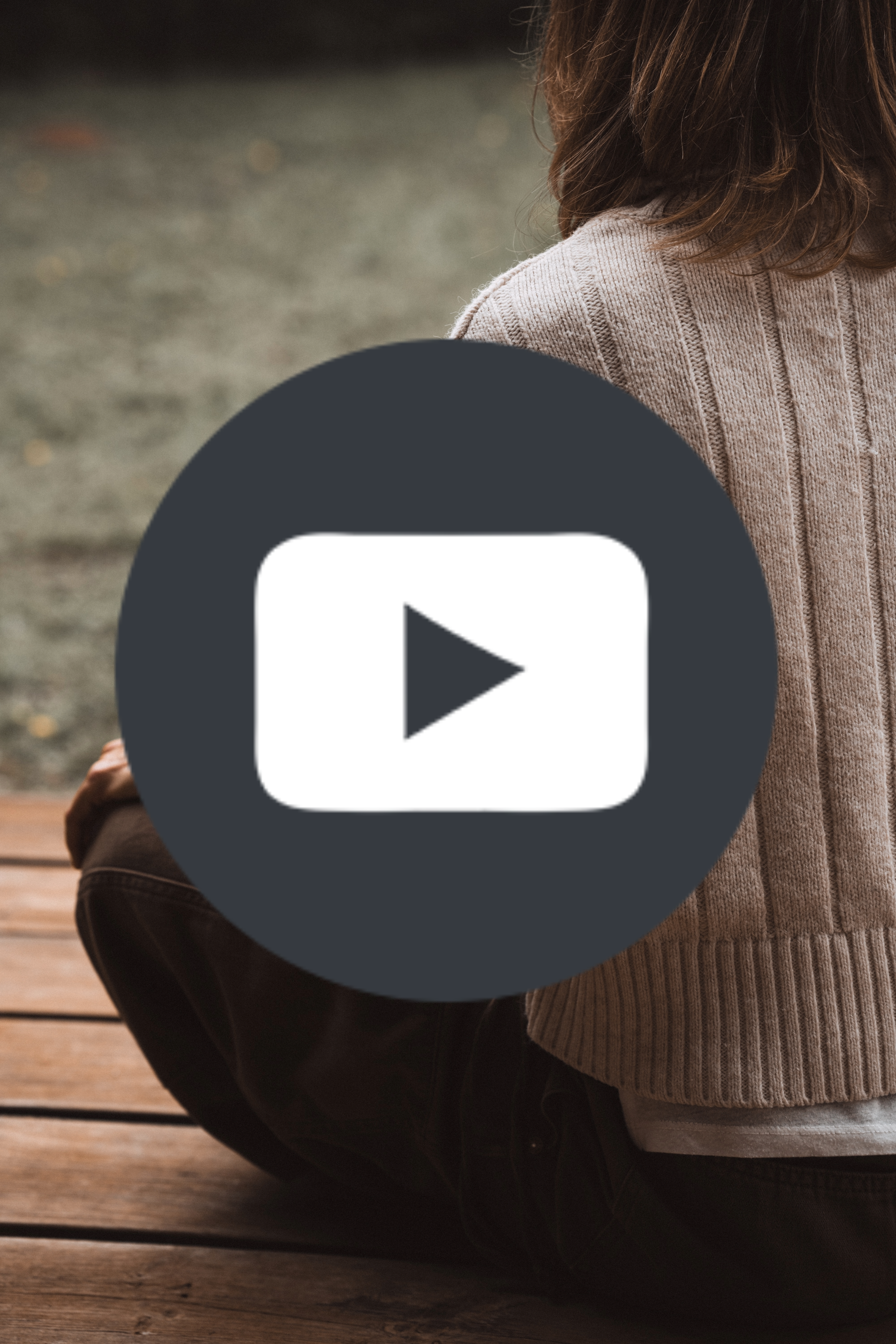 Person sitting on a wooden deck wearing a beige sweater, with a blurred outdoor background.