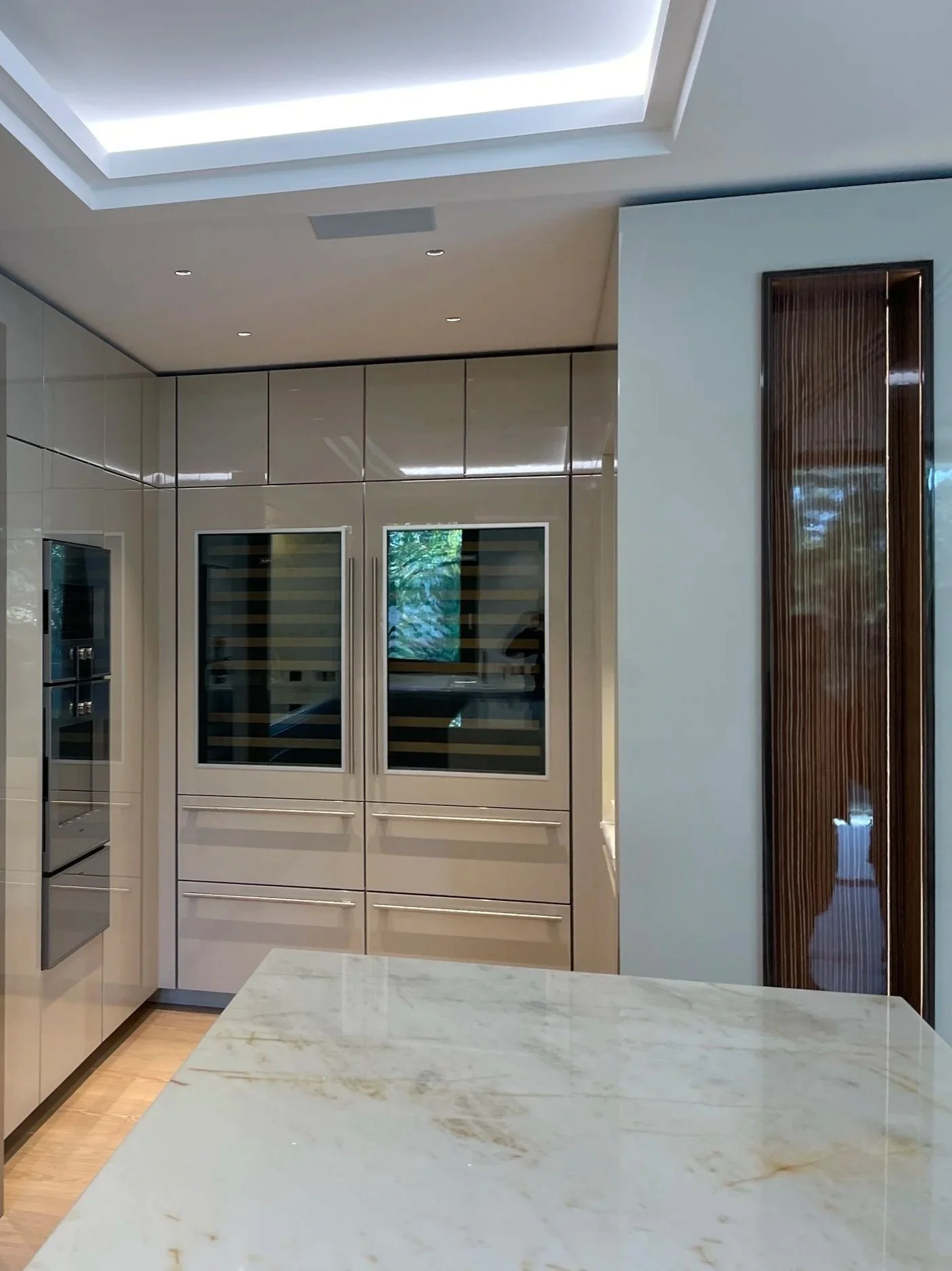 Cuisine moderne avec un plafond lumineux, des appareils encastrés, un comptoir en marbre et des armoires en verre