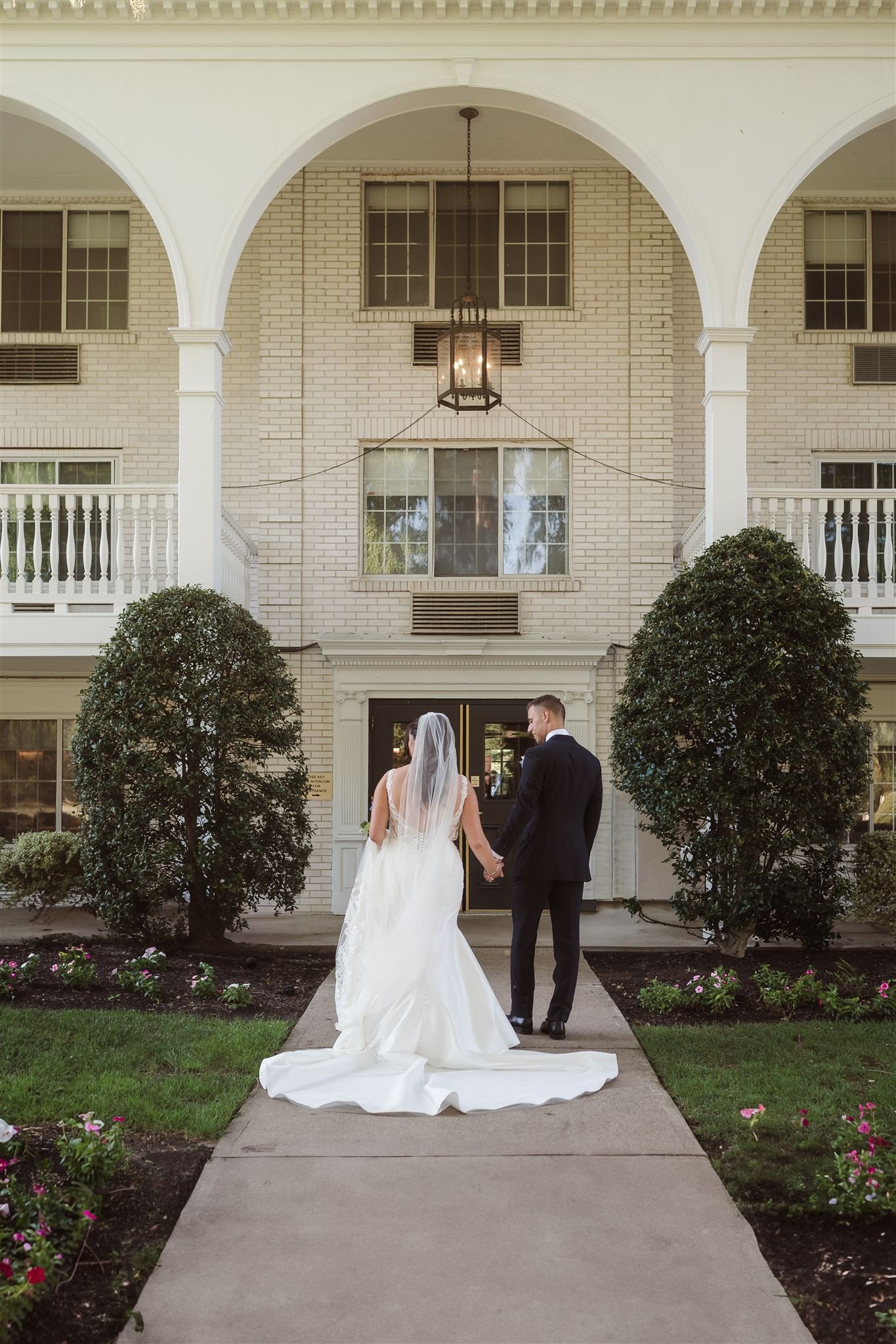 Bride and groom holding hands walking toward building entrance at wedding venue.