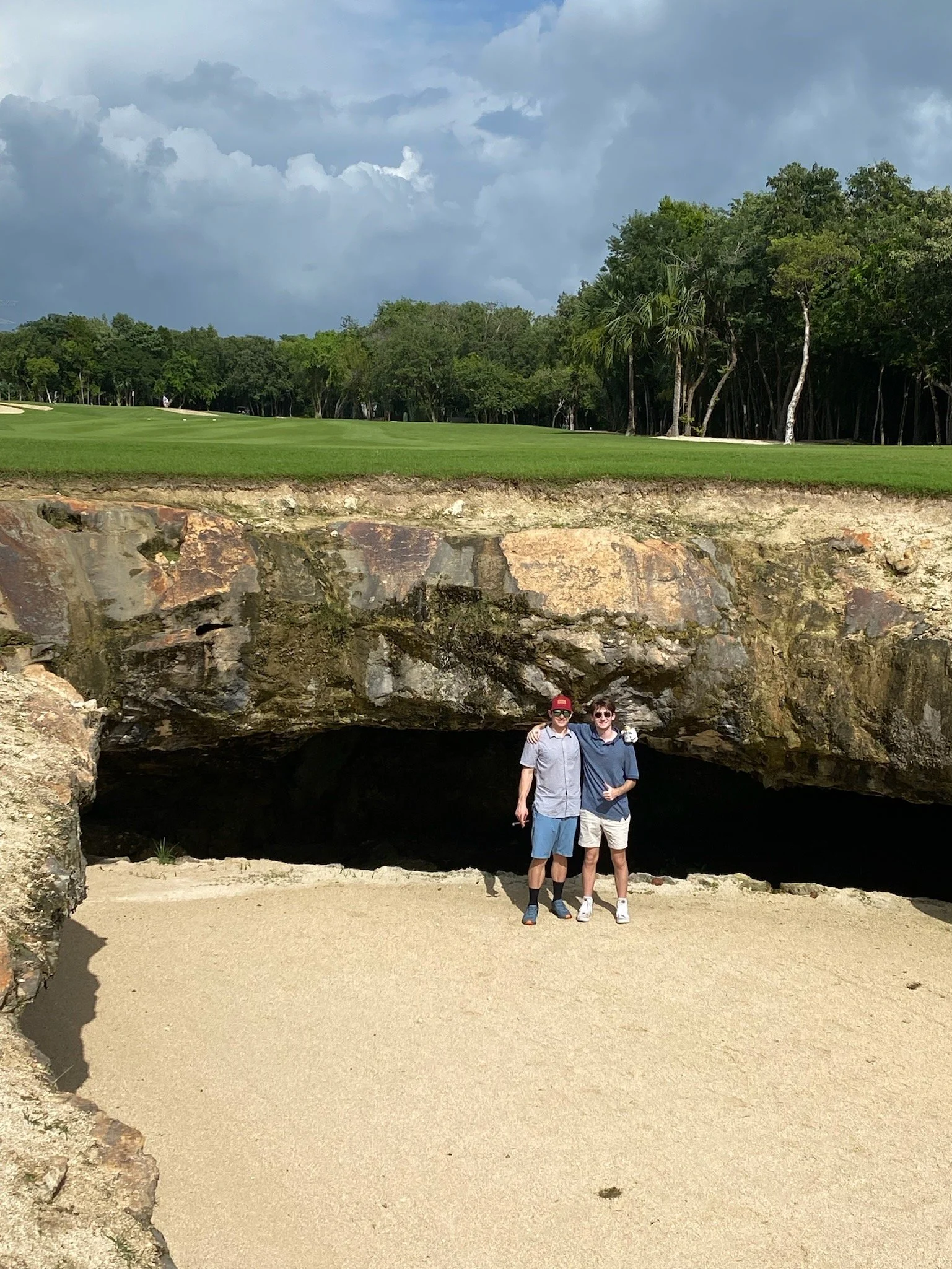Joseph posing in front of a cenote on a golf course with his cousin. 
