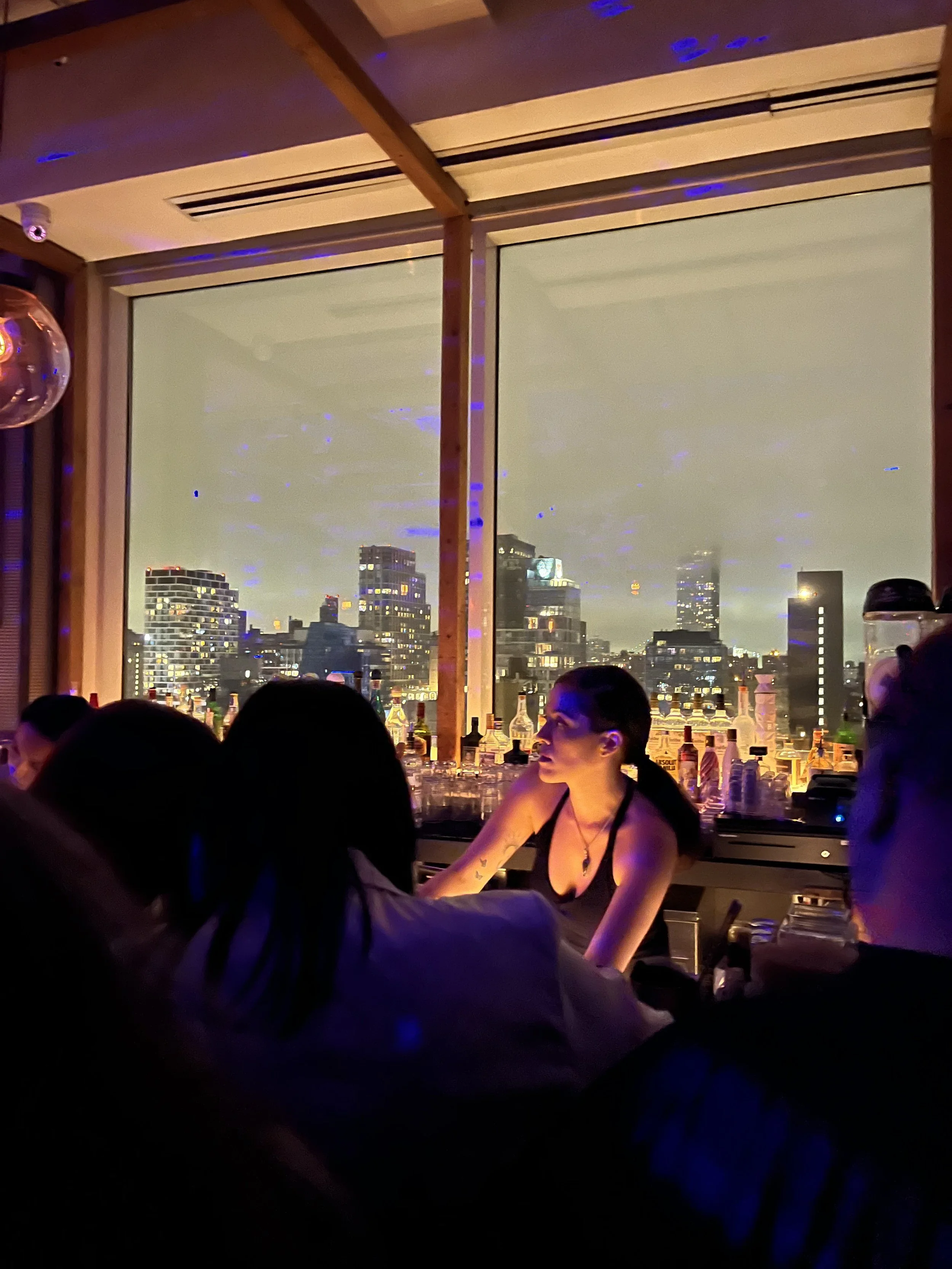 View of the bartender with the Brooklyn skyline behind her during a night out in East Village.