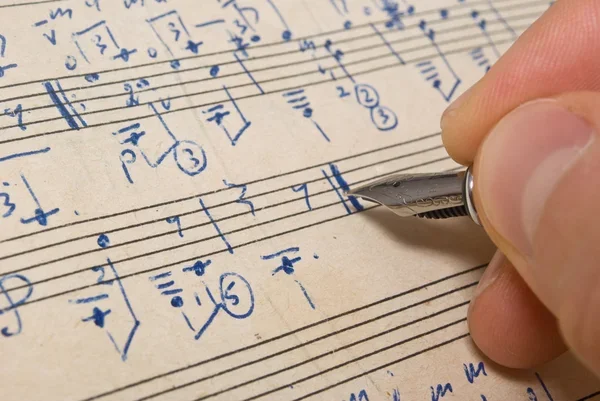 A hand writing musical notation with a pen on sheet music paper.