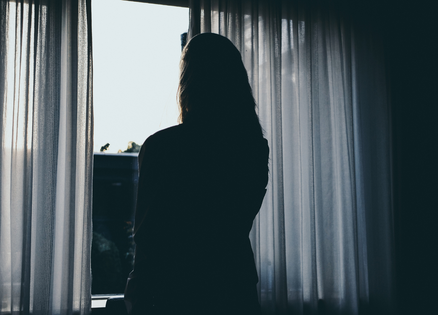 Woman looks out window alone in her relationship, feels unheard and unseen, no voice in relationship