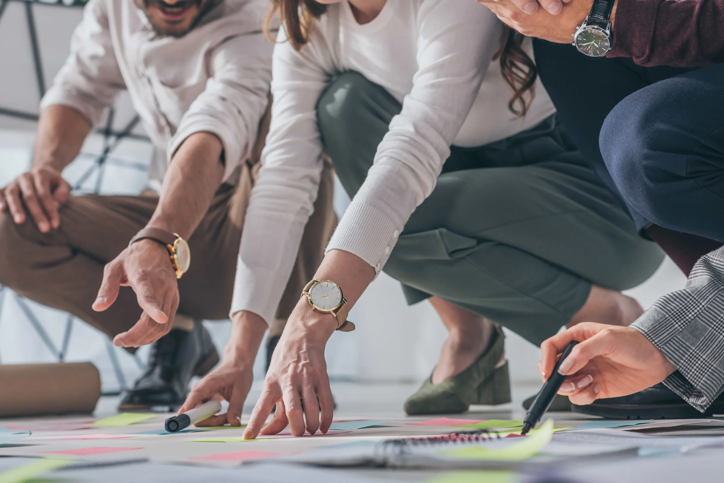 People collaborating on a project, kneeling on the floor with notes and markers.
