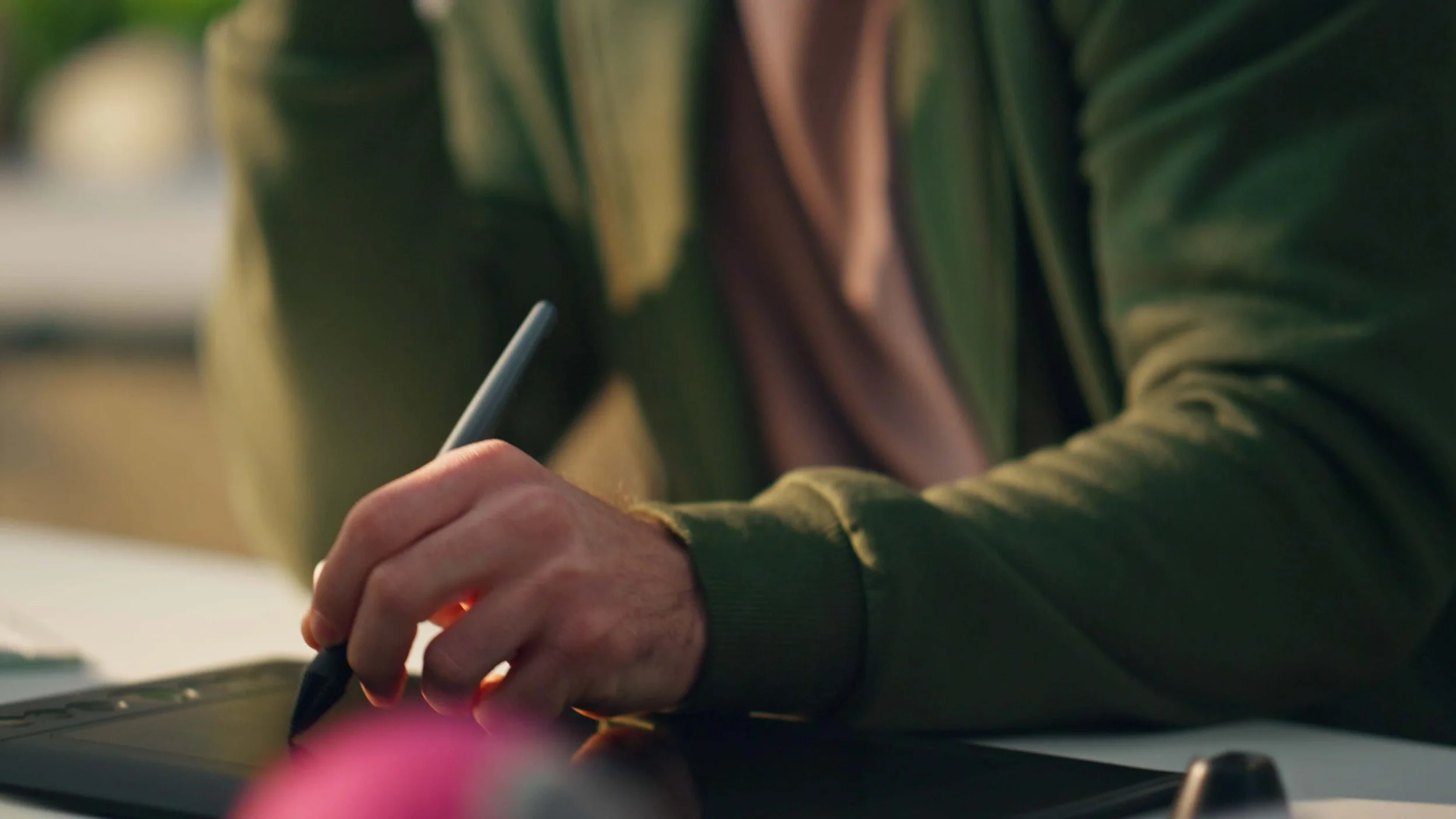 Person in a green jacket drawing or writing on a touchscreen tablet with a stylus.