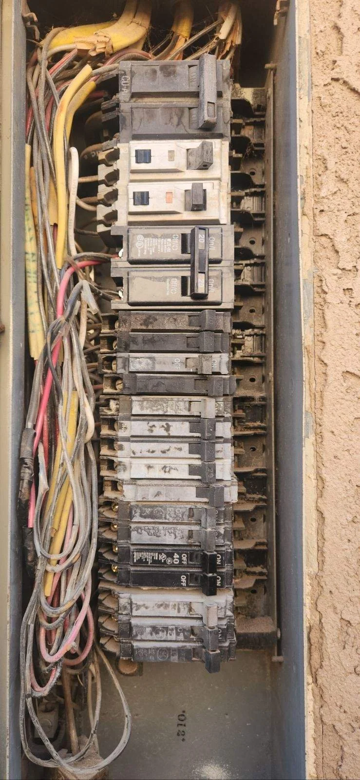 Close-up of an old, dusty electrical circuit breaker panel with multiple switches and tangled wires.