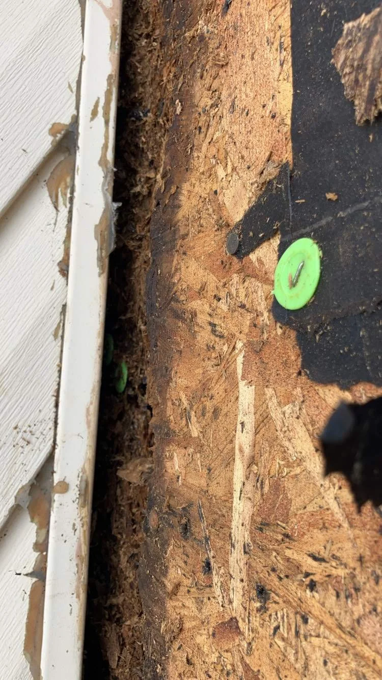 Close-up of a damaged floor with exposed plywood, debris, and a green plastic cap with a metal checkmark on it.