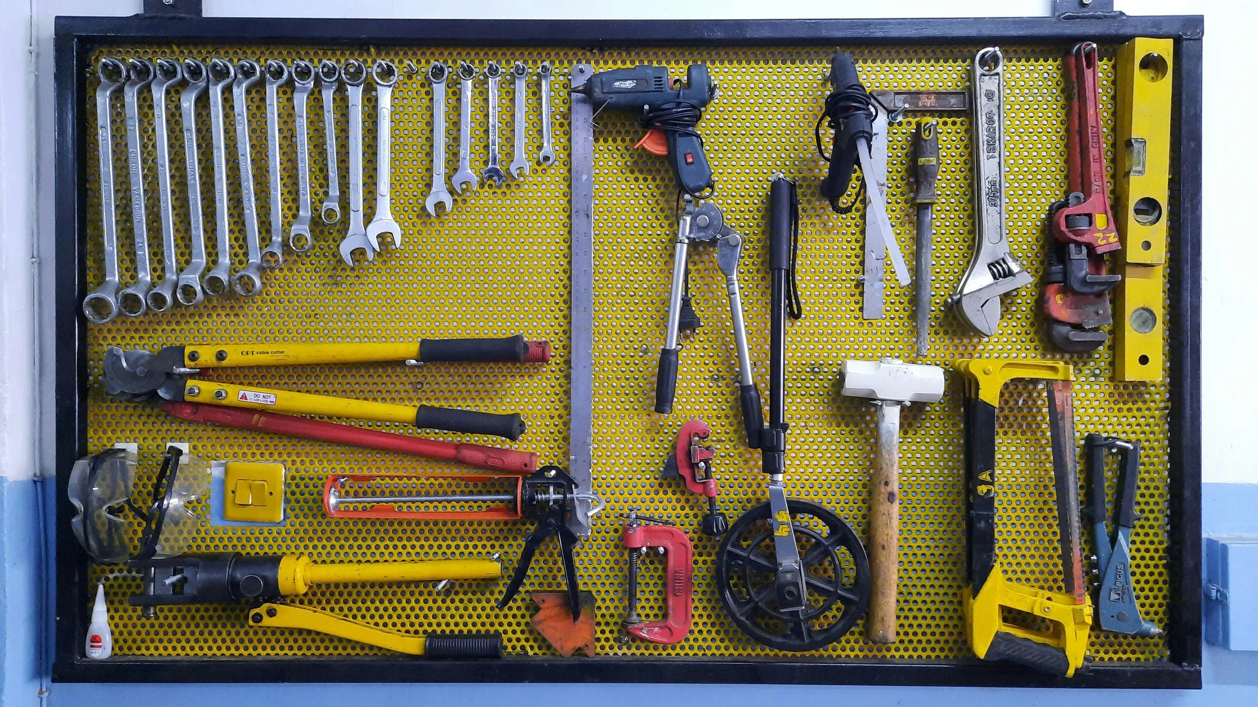 A yellow tool storage board with various hand tools including wrenches, pliers, screwdrivers, a hacksaw, a hammer, a circular saw, and a level, neatly organized and hanging on the board.