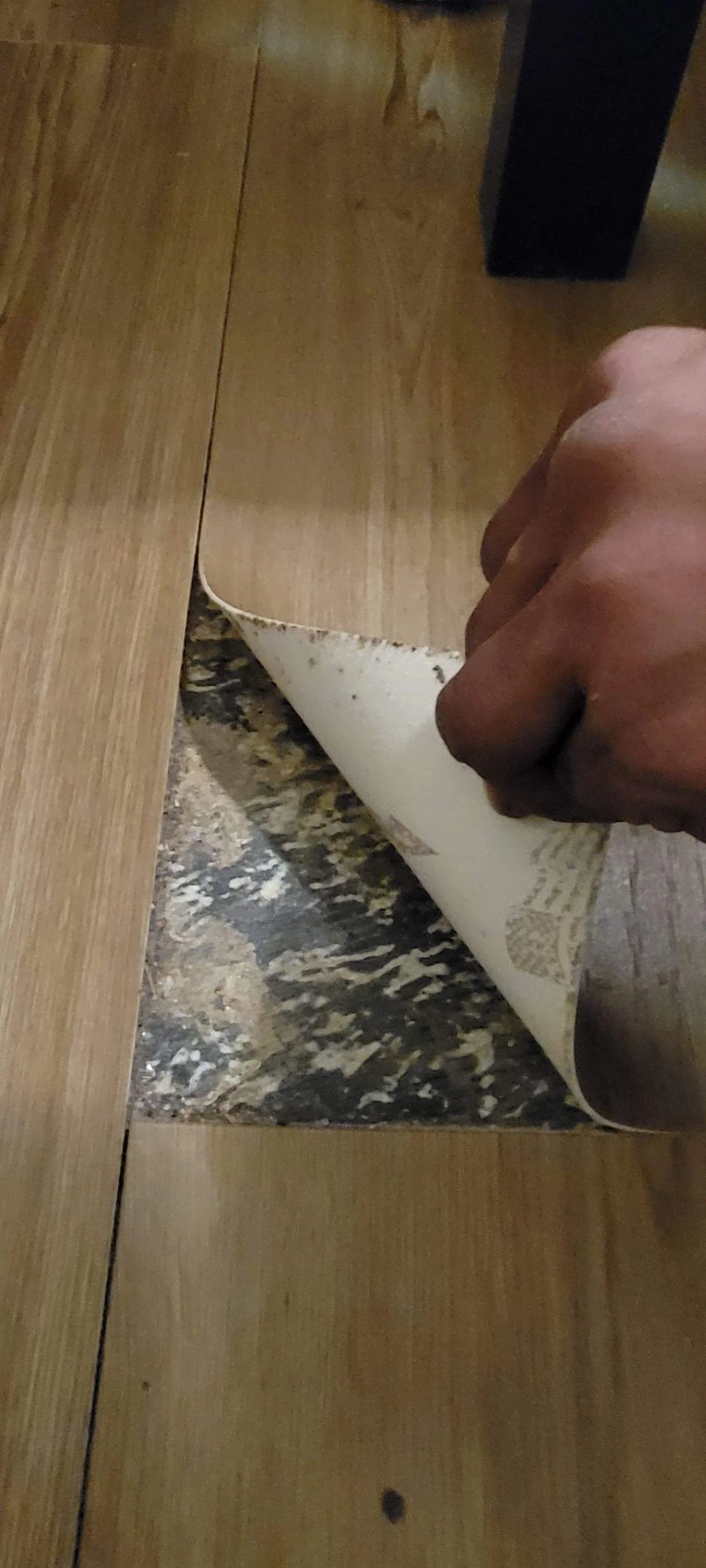 A person peeling back a corner of a wooden table to reveal the surface underneath, which has black and beige marble pattern.