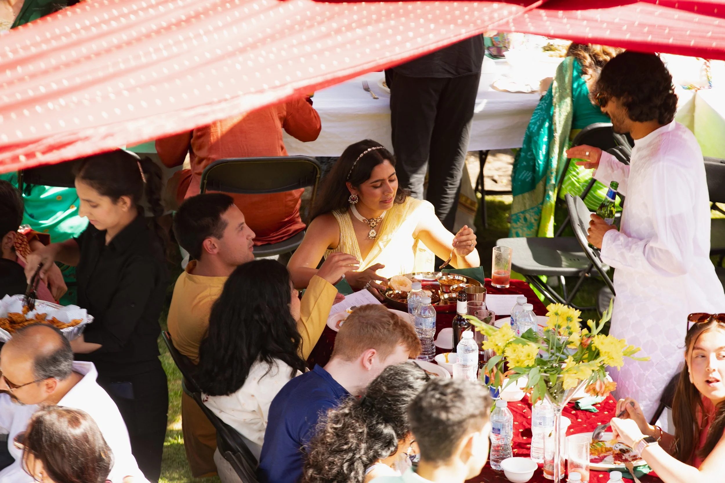 People enjoying an outdoor Indian celebration with traditional clothing, food, and decorations under a tent.
