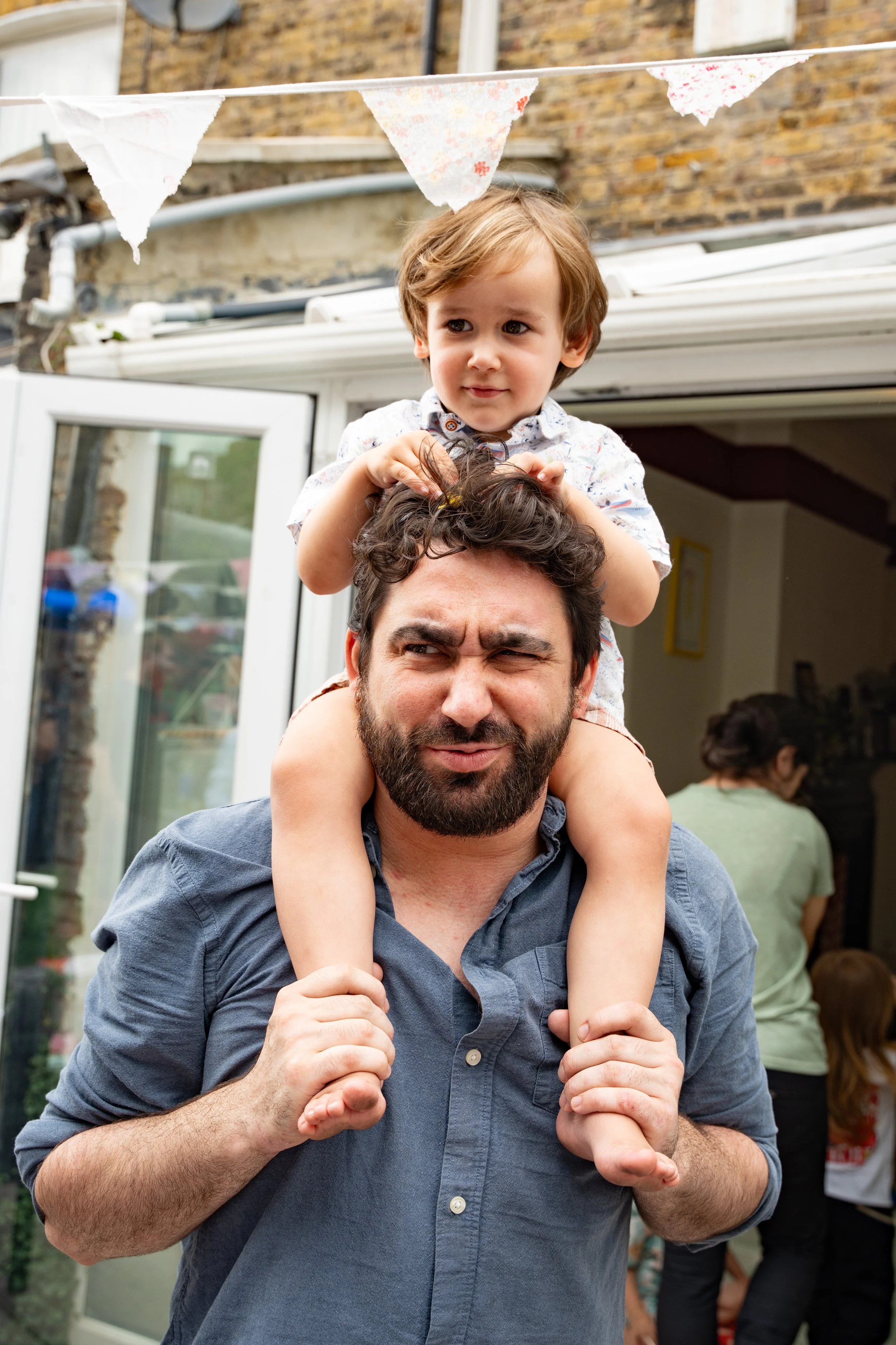 A man carrying a young boy on his shoulders outdoors during a gathering or celebration.
