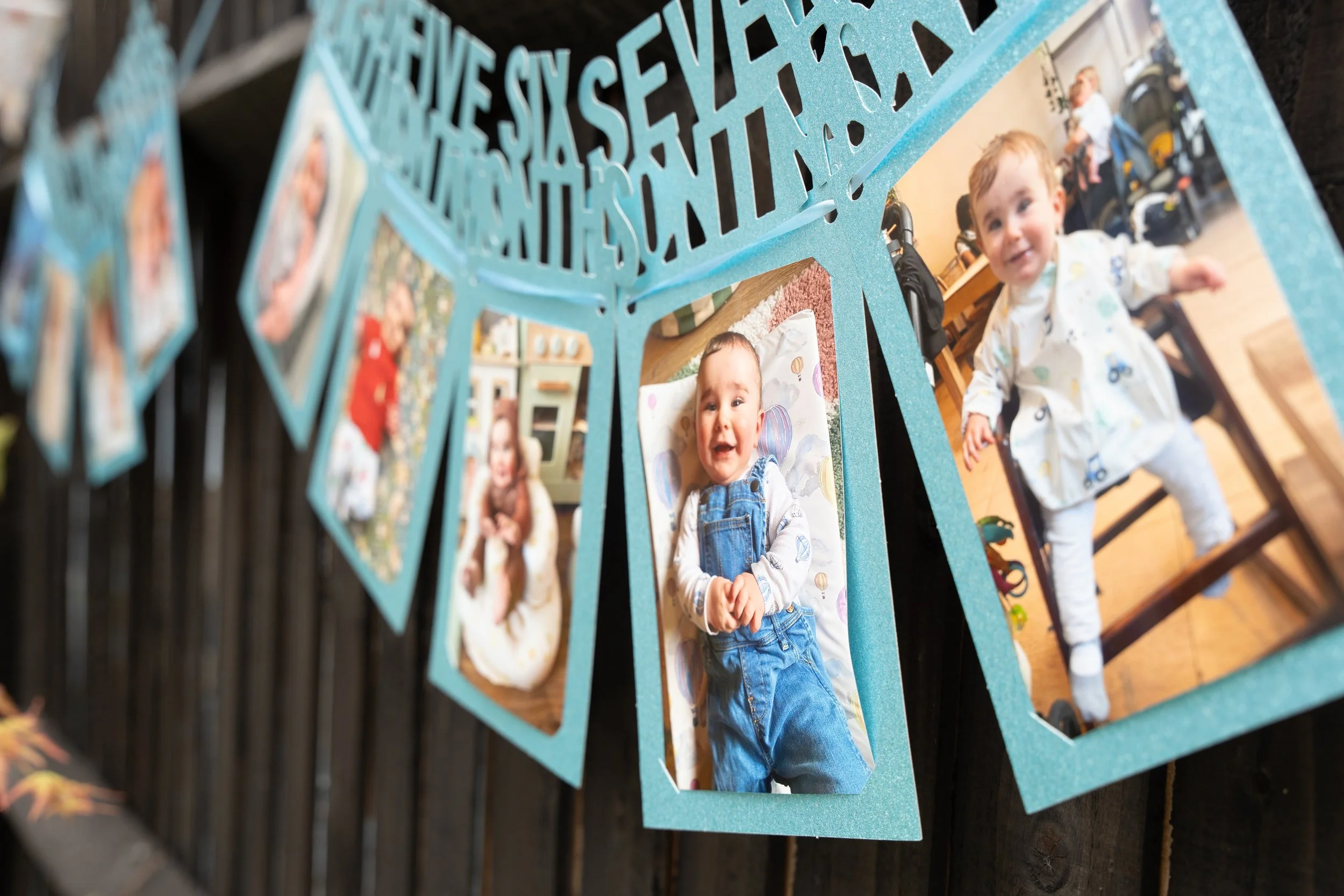 A photo display of several photographs of a young child, with some of the pictures showing the child smiling and standing, all framed with blue borders and hanging from a string.