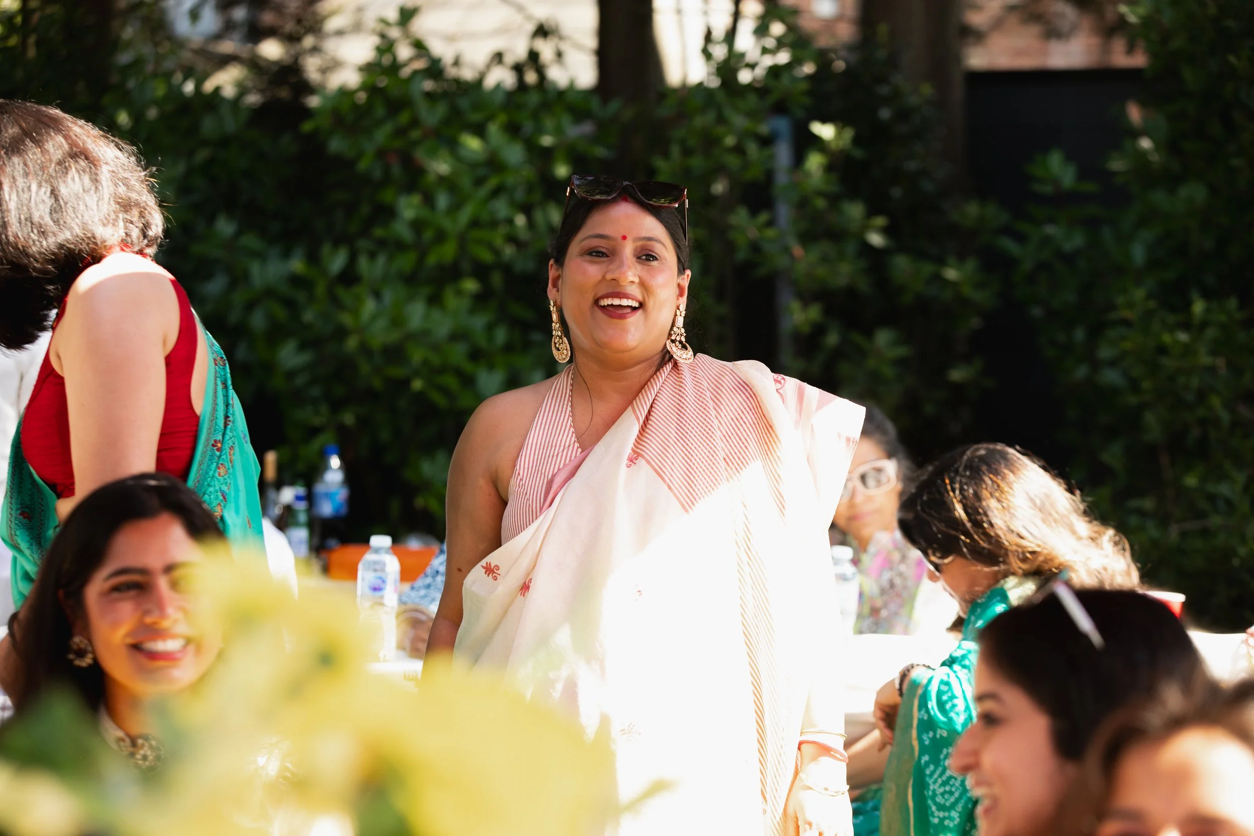Woman in traditional Indian attire smiling and interacting with guests at an outdoor gathering.