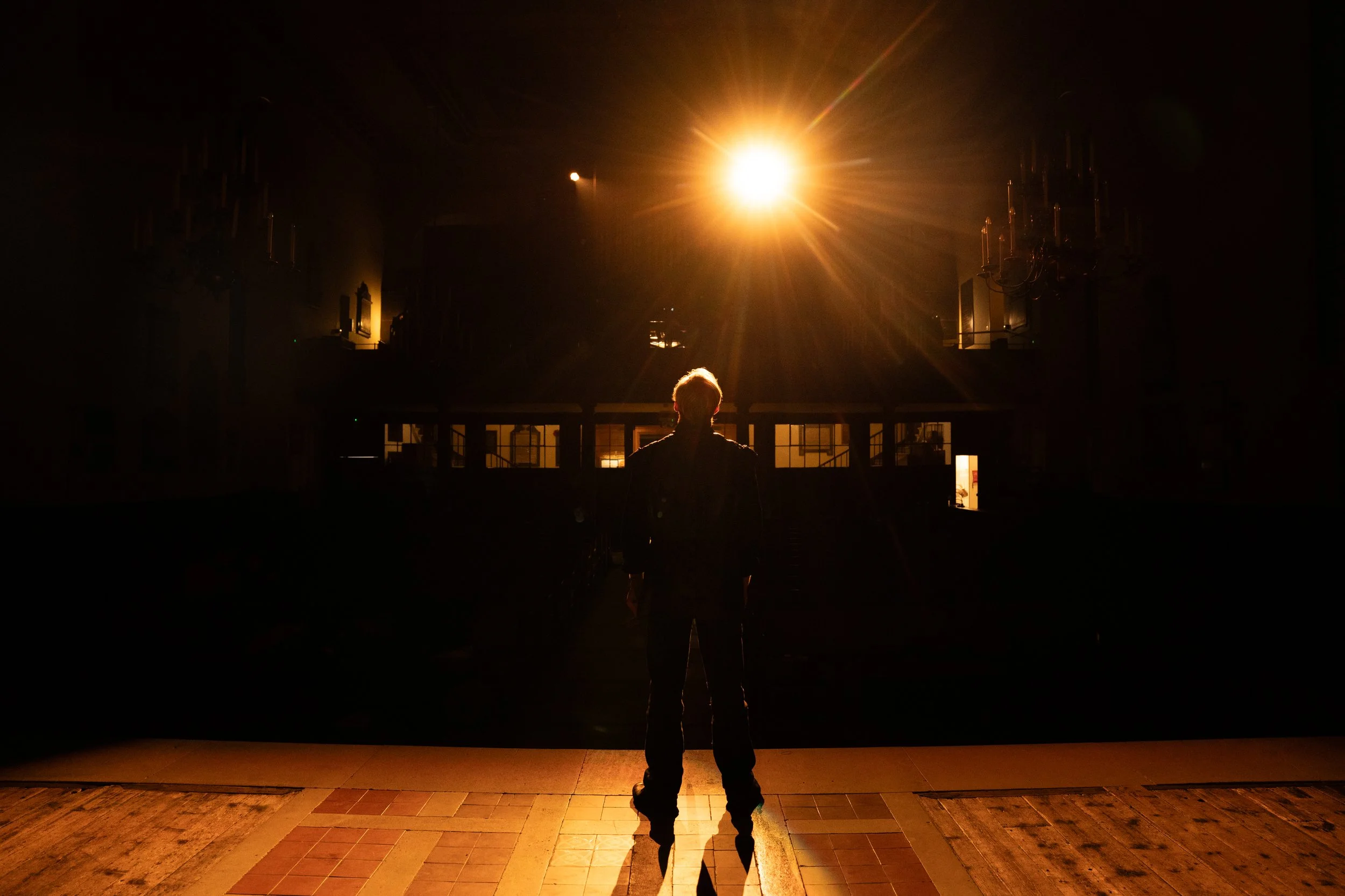 A silhouette of a person standing in front of a large bright light source at night, with dark buildings in the background.