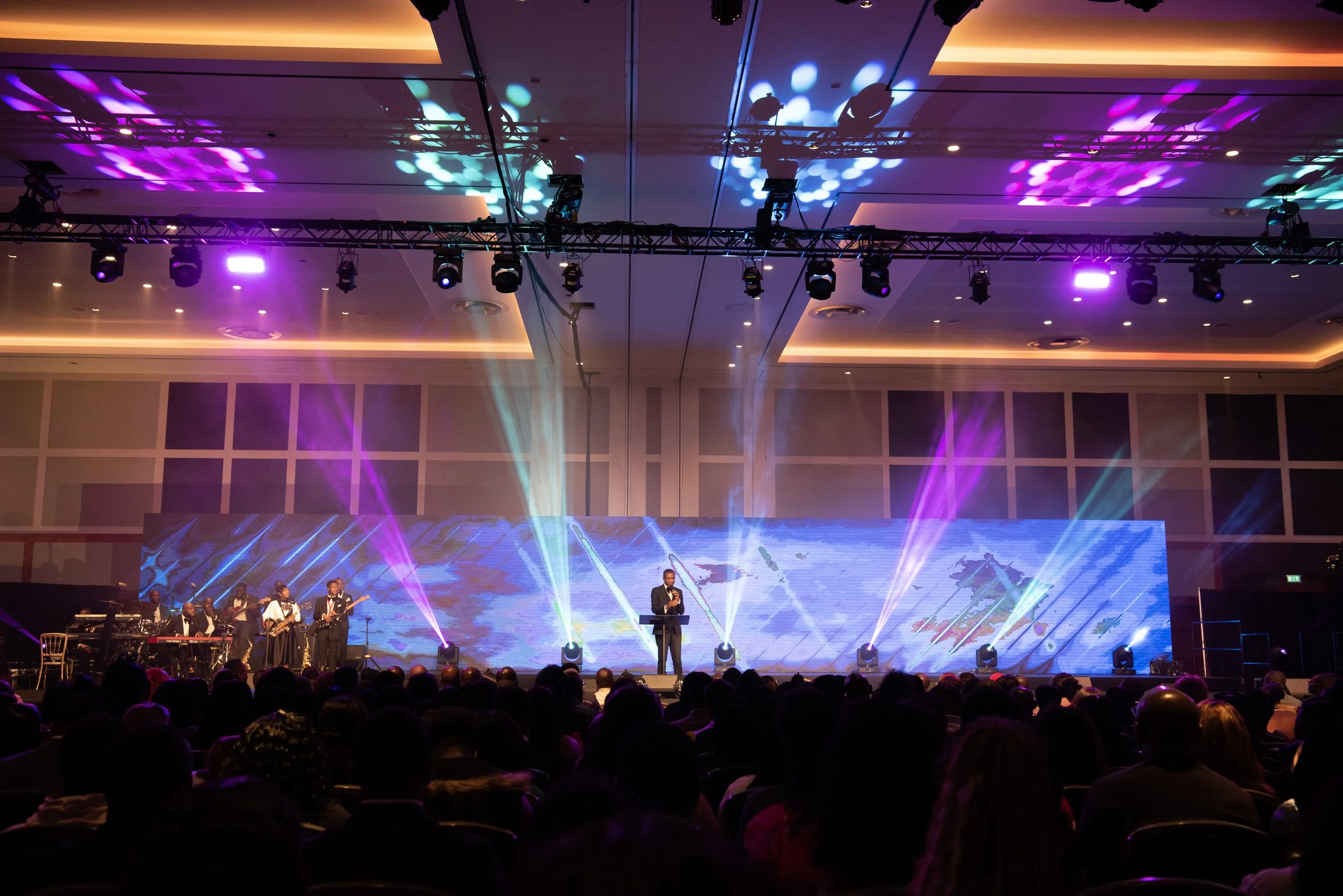 Stage with a band performing, colorful lighting, and an audience at an indoor event