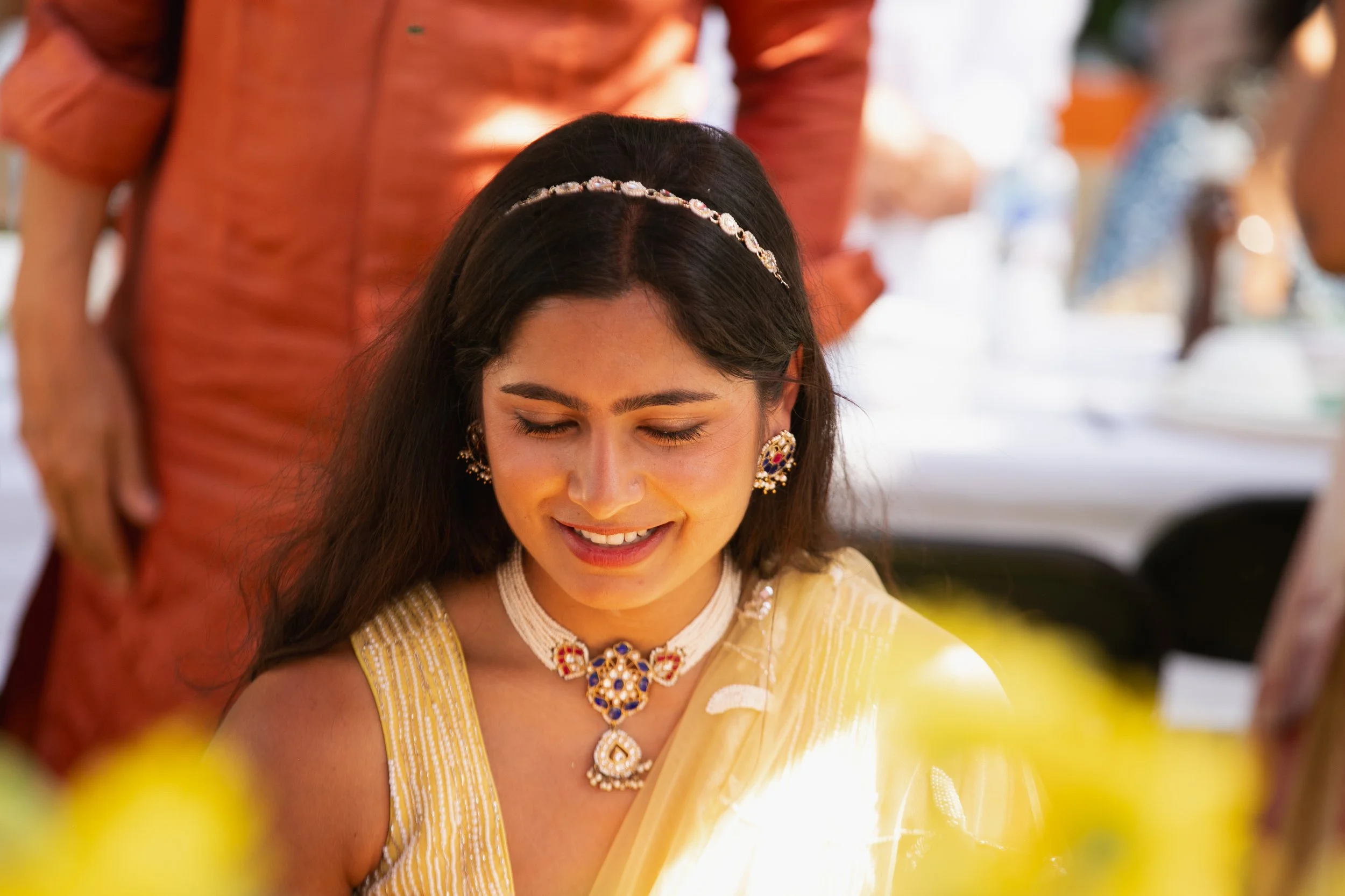 A woman dressed in traditional Indian attire and jewelry, smiling with her eyes closed at a festive event.