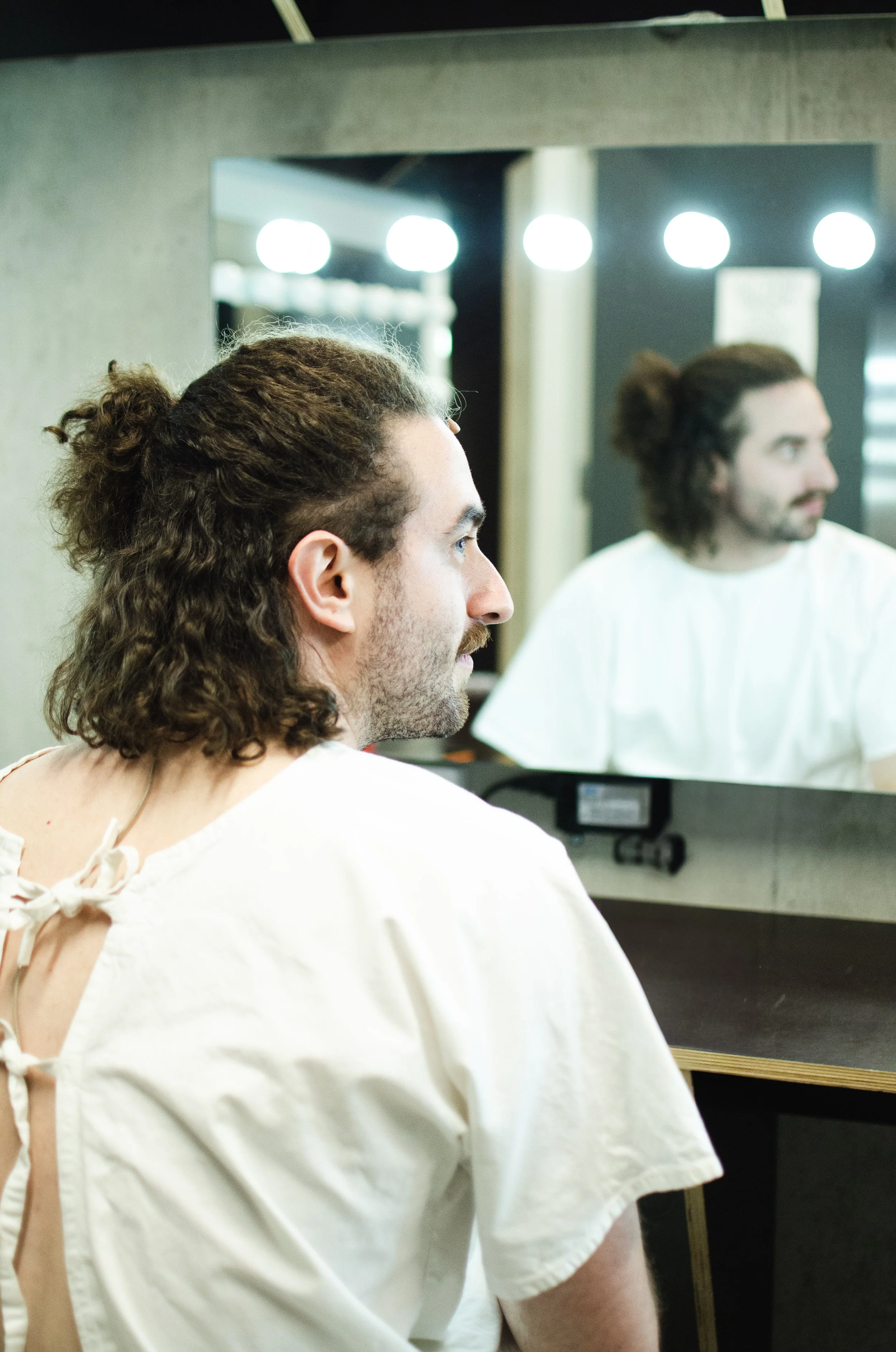 A man with curly hair and a beard looking at his reflection in a mirror in a hair salon or barbershop.