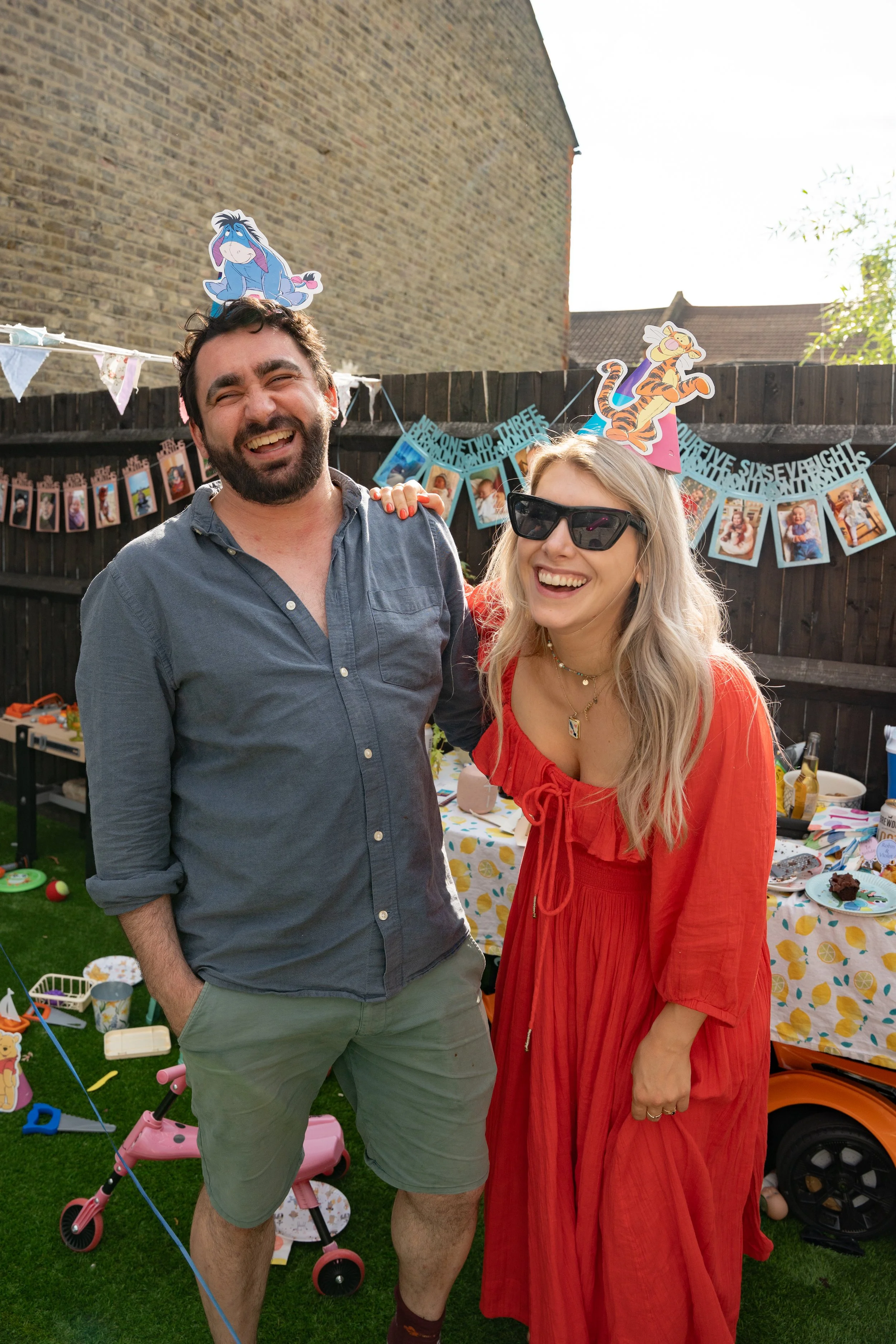 Two people smiling and laughing at an outdoor birthday party, wearing themed headbands and posing together.