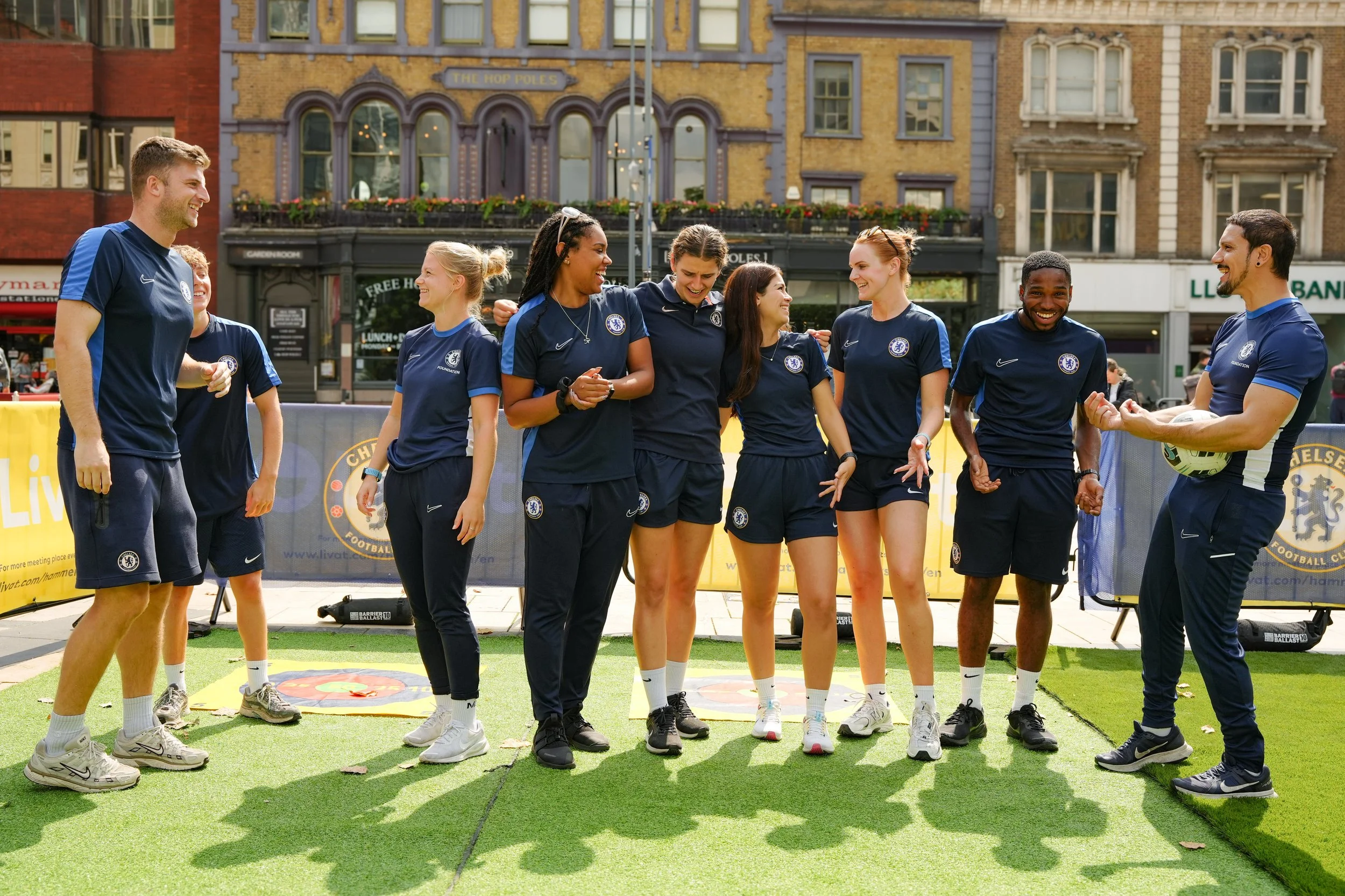 Group of female and male soccer players in blue uniforms standing together outdoors, celebrating and smiling.