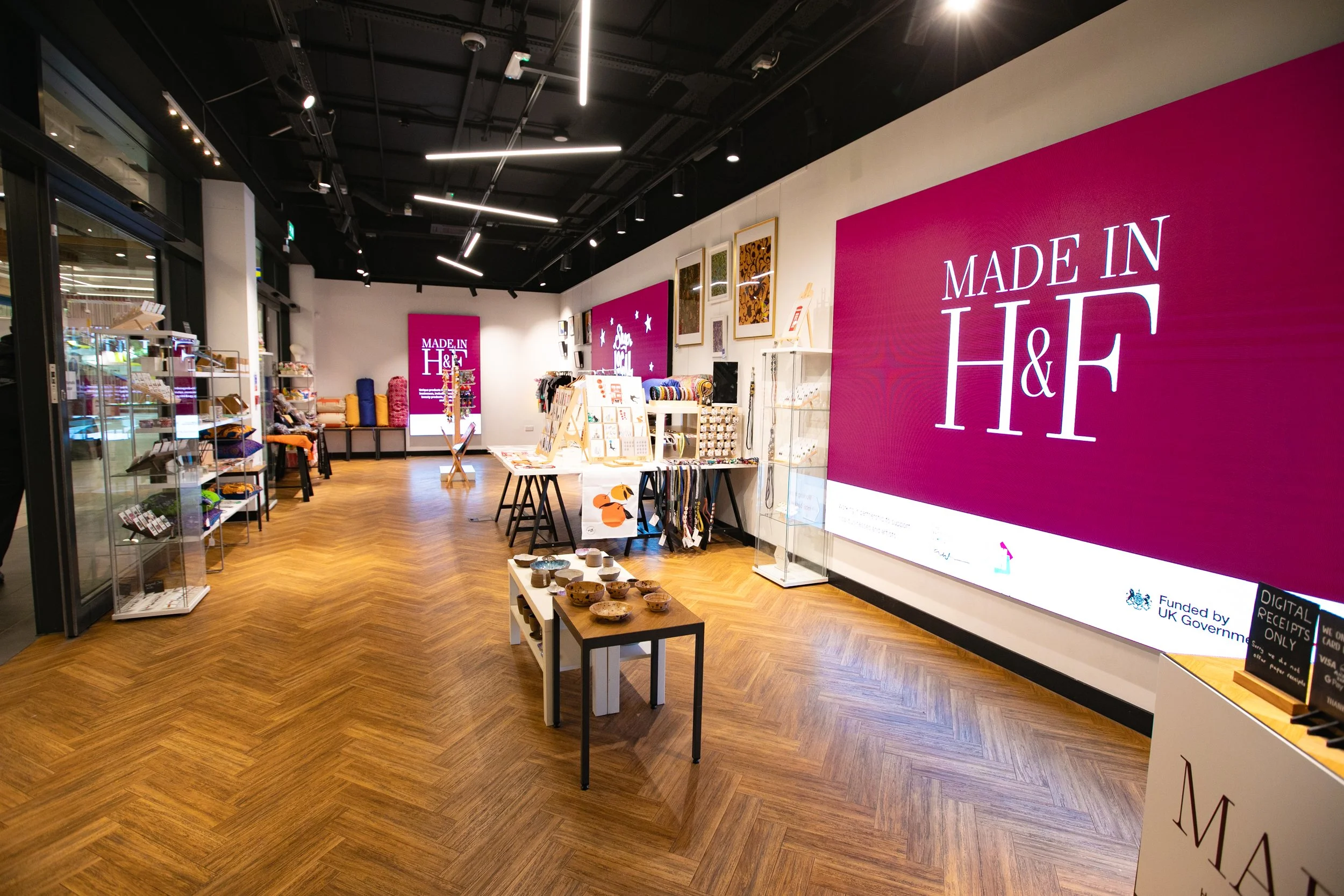 Interior of a retail store with wooden flooring, displaying colorful home decor, jewelry, and accessories, with a large pink sign reading 'Made in H&F' on the wall.