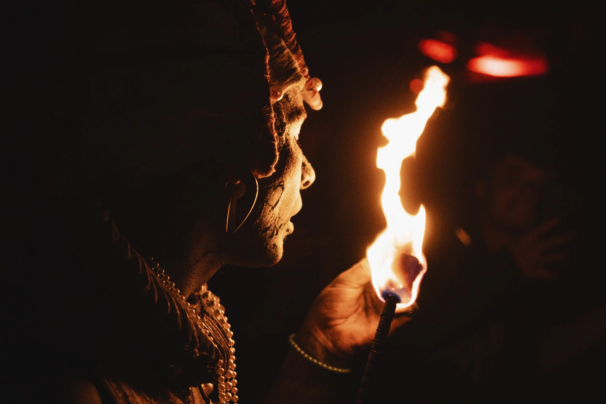 Person with traditional jewelry and face paint holding a fire torch at night.