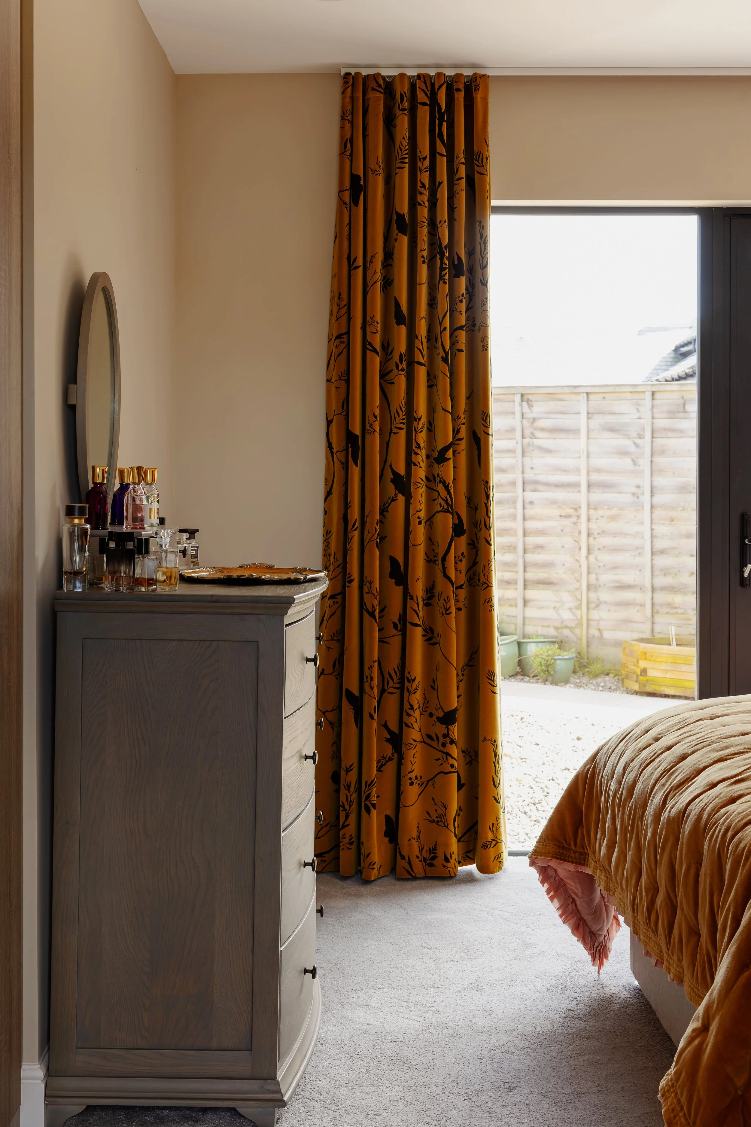 Warm bedroom interior with mustard patterned curtains, wooden chest of drawers and layered textiles, styled at The Dairy.